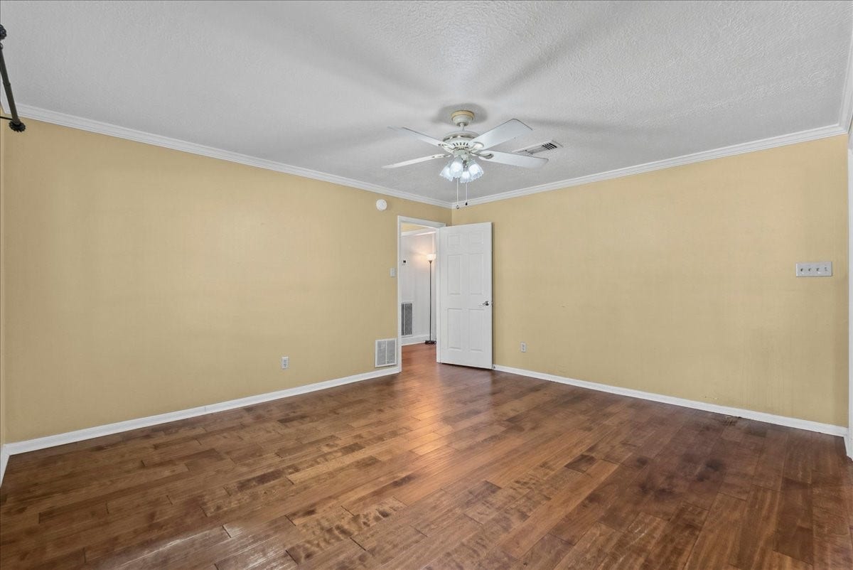 The primary bedroom features warm wood flooring, soft yellow walls, and a ceiling fan, offering a cozy and inviting retreat.
