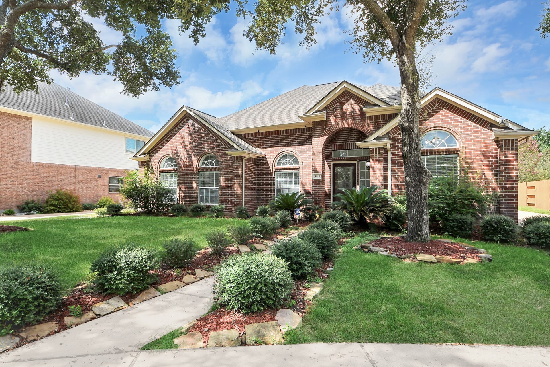 5815 Pheasant Ridge Lane, Houston, TX 77041 Charming brick home with beautiful arched windows, nestled in a lush landscaped garden featuring mature trees and manicured shrubs for added curb appeal.