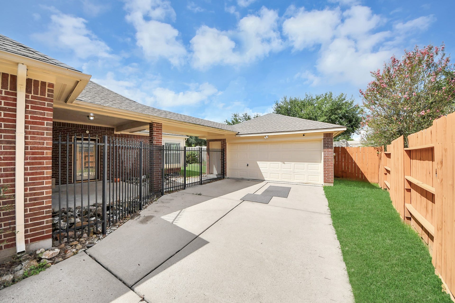5815 Pheasant Ridge Lane, Houston, TX 77041 Spacious driveway leading to a two-car garage, complemented by a fenced side area and lush greenery, perfect for privacy and convenience.
