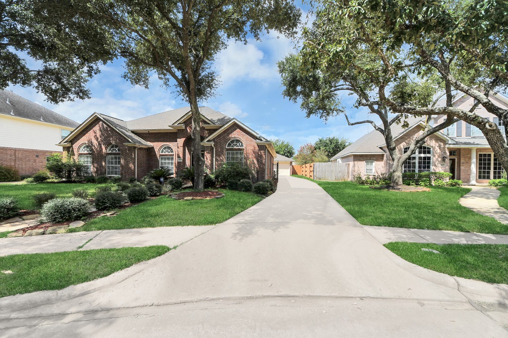 5815 Pheasant Ridge Lane, Houston, TX 77041 Charming brick home with elegant arched windows, nestled among mature trees and lush landscaping, featuring a wide driveway leading to a detached garage.