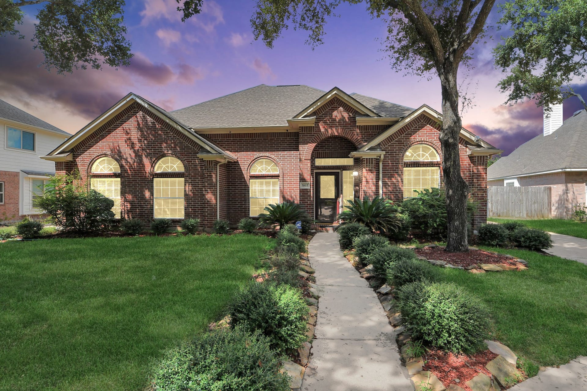 5815 Pheasant Ridge Lane, Houston, TX 77041 Charming brick home with a welcoming pathway, lush landscaping, and elegant arched windows, set against a picturesque sky.