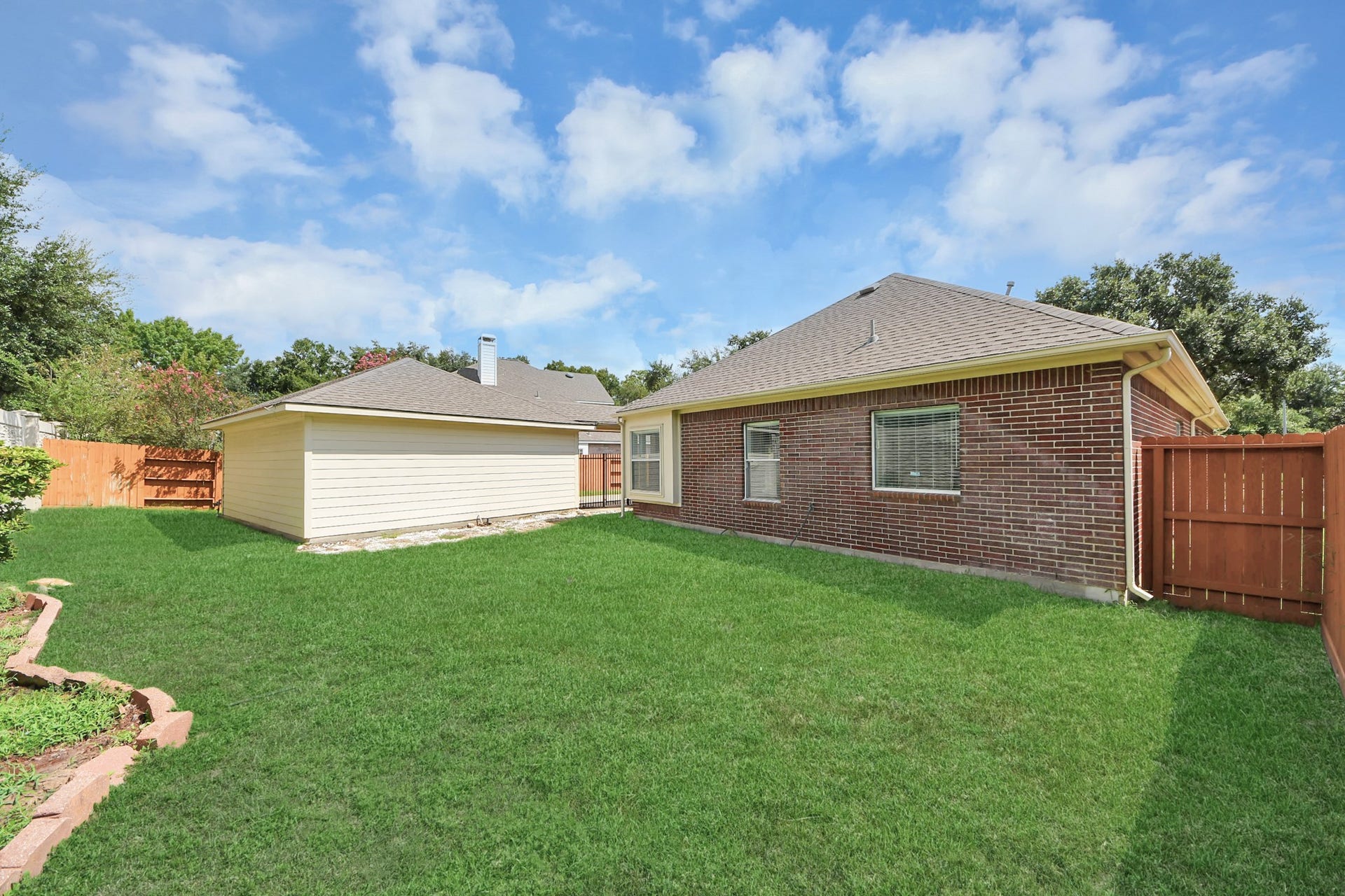 5815 Pheasant Ridge Lane, Houston, TX 77041 Spacious backyard with lush green lawn, bordered by a charming red brick exterior and a wooden fence for added privacy.