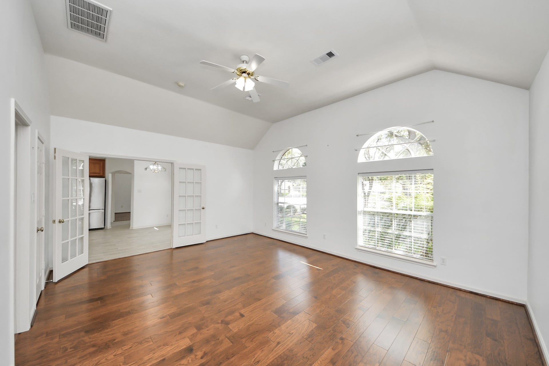 5815 Pheasant Ridge Lane, Houston, TX 77041 Spacious living area featuring elegant hardwood floors, abundant natural light from large arched windows, and a ceiling fan for comfort, seamlessly connected to the kitchen through stylish French doors.