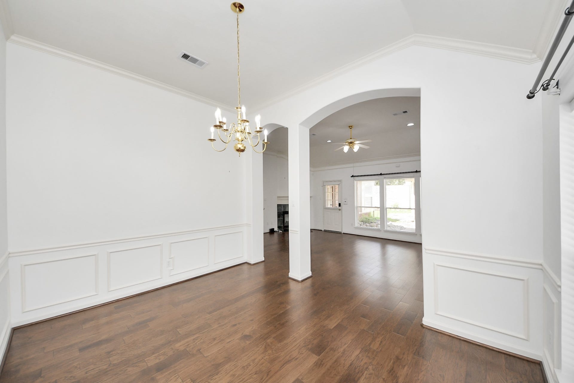 5815 Pheasant Ridge Lane, Houston, TX 77041 Elegant dining area with hardwood floors, wainscoting, and a classic chandelier, flowing seamlessly into a bright living space with large windows.