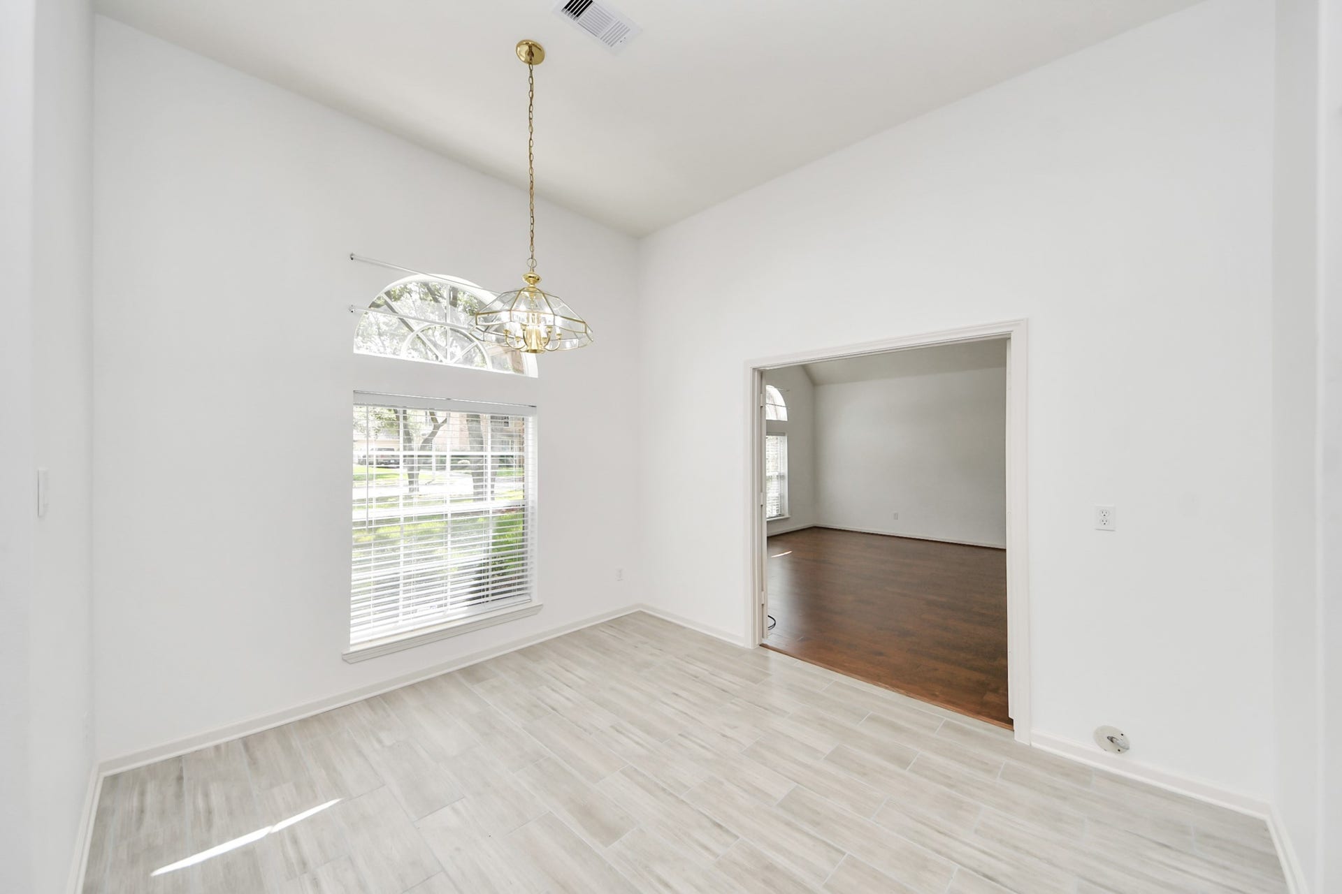 5815 Pheasant Ridge Lane, Houston, TX 77041 Bright and inviting living space featuring elegant tile flooring, a large arched window for natural light, and a stylish chandelier, seamlessly connecting to a cozy adjoining room with warm wood floors.