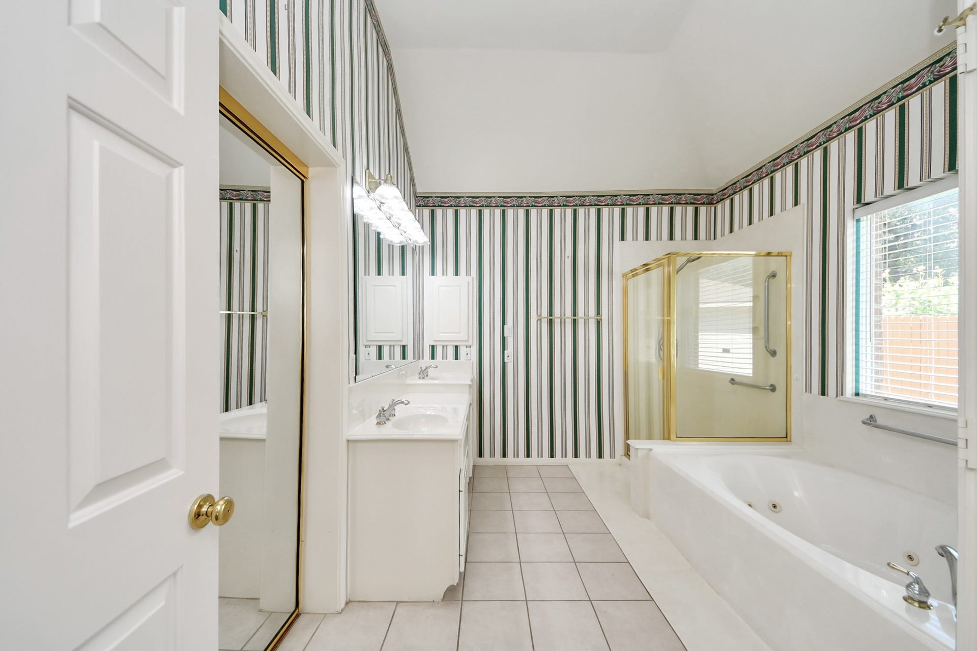 5815 Pheasant Ridge Lane, Houston, TX 77041 Spacious bathroom featuring a luxurious jetted tub, separate glass-enclosed shower, dual sinks, and elegant striped wallpaper.