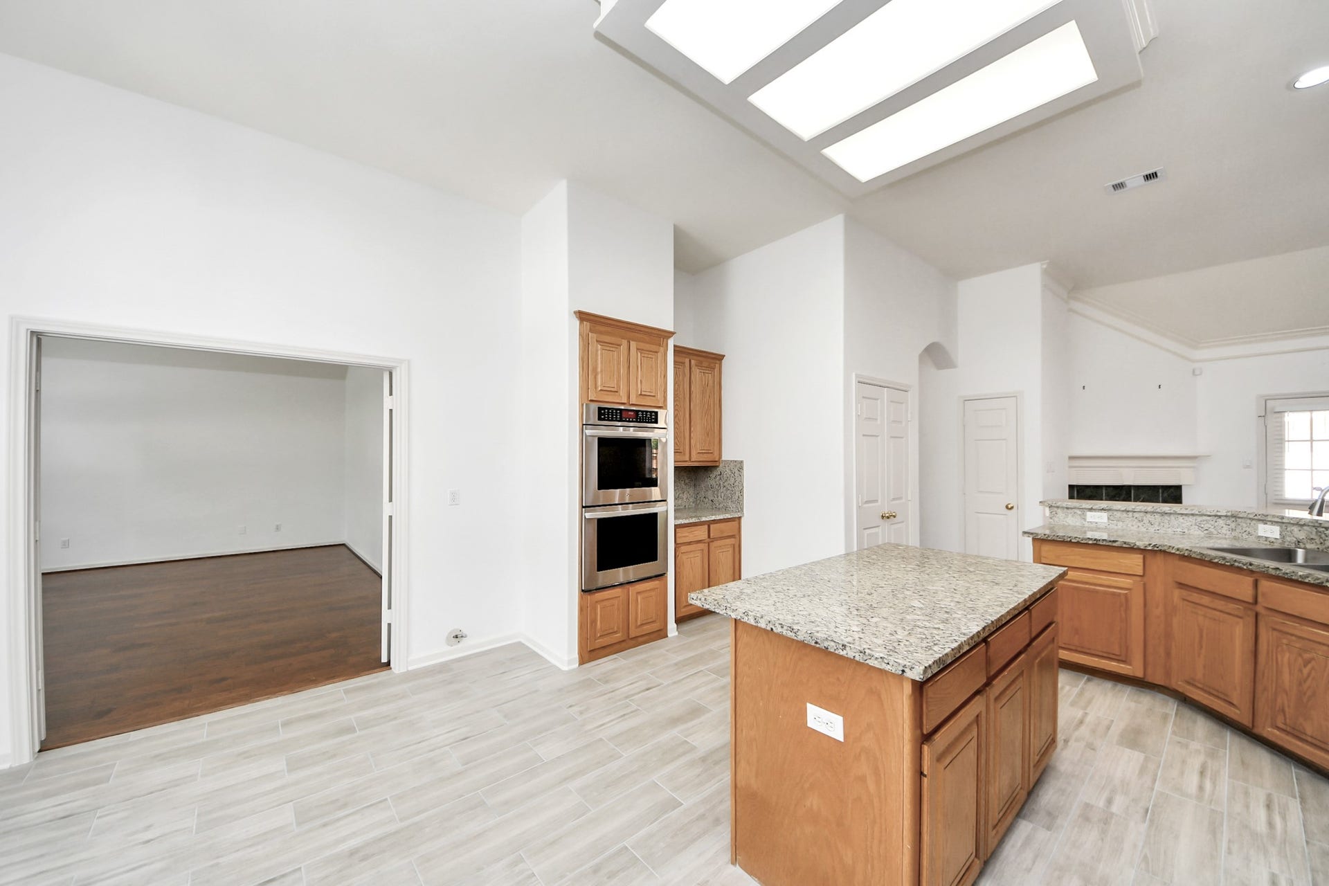 5815 Pheasant Ridge Lane, Houston, TX 77041 Spacious kitchen with granite countertops and wood cabinetry, featuring a central island and stainless steel appliances. Adjacent open living area with hardwood floors offers a seamless flow for entertaining.