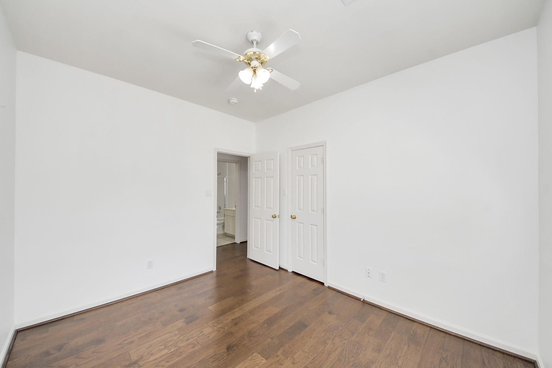 5815 Pheasant Ridge Lane, Houston, TX 77041 Bright room with elegant hardwood floors, a classic ceiling fan, and a seamless flow into an adjoining bathroom through double doors.