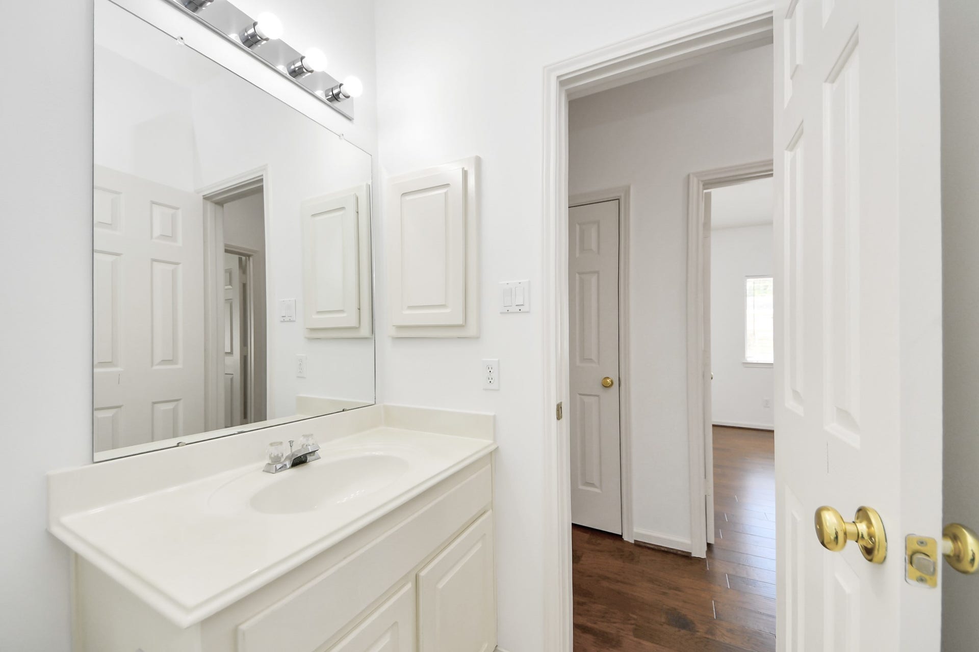 5815 Pheasant Ridge Lane, Houston, TX 77041 Bright bathroom features a sleek vanity with ample storage, modern lighting, and a large mirror, leading into a hallway with wood flooring.