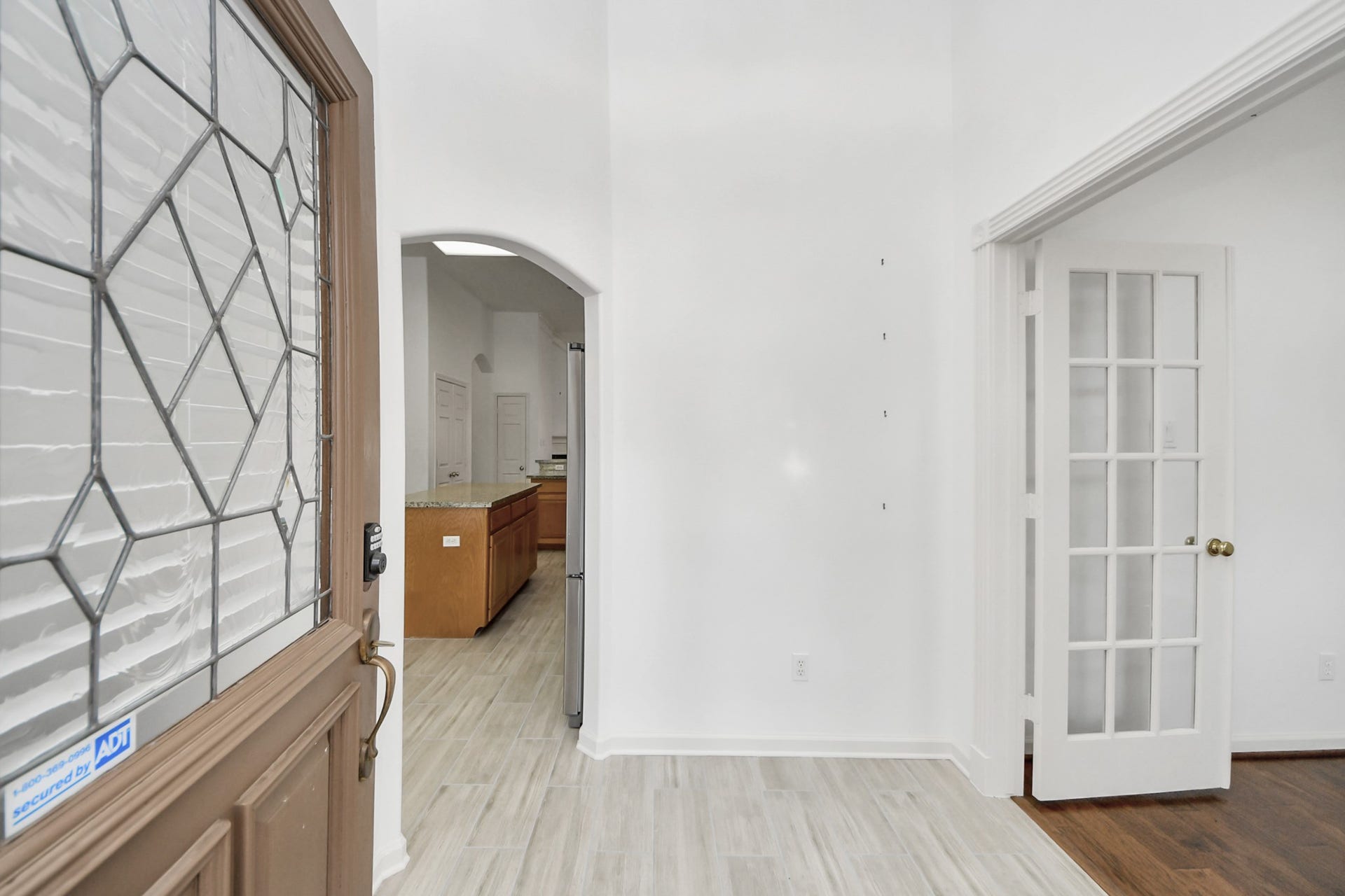 5815 Pheasant Ridge Lane, Houston, TX 77041 Inviting entryway with a decorative glass front door, leading to a bright interior featuring elegant French doors and a glimpse of the spacious kitchen with warm wood cabinetry and granite countertops.