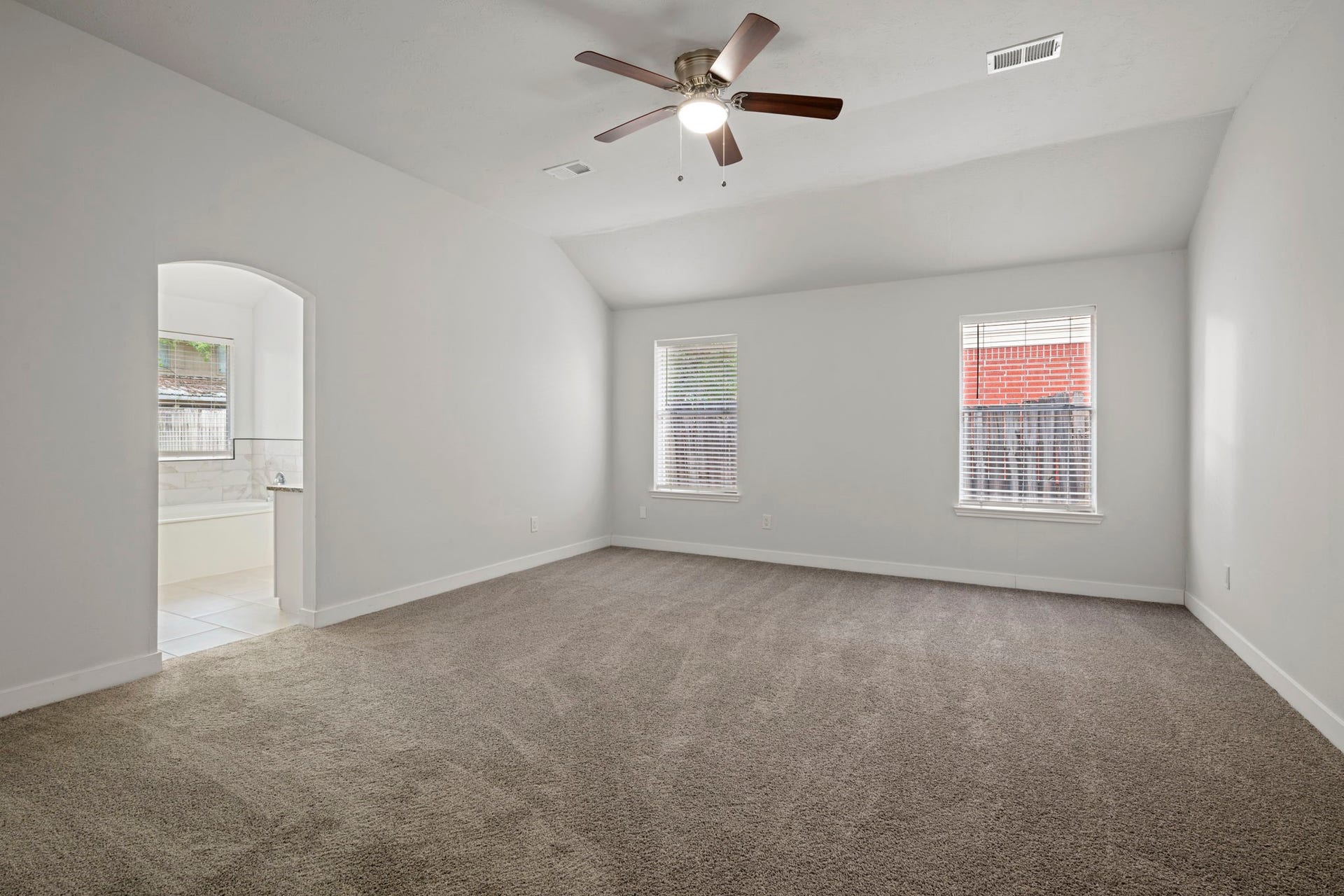 Spacious bedroom with plush carpet, large windows for natural light, and an elegant ceiling fan, leading to an en-suite bathroom with a soaking tub.