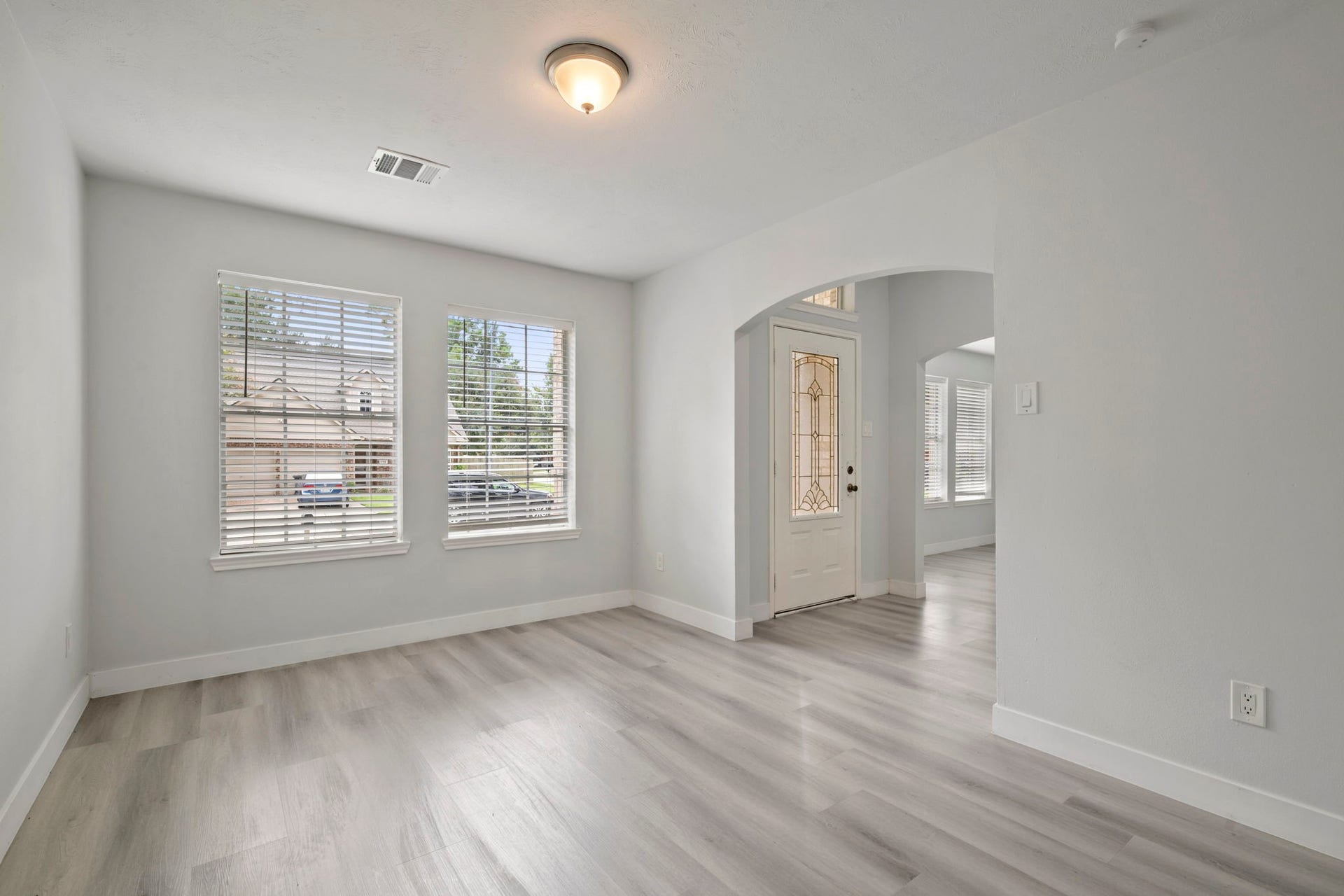 Bright and welcoming entryway with elegant light wood flooring, large windows for natural light, and a beautifully detailed front door.