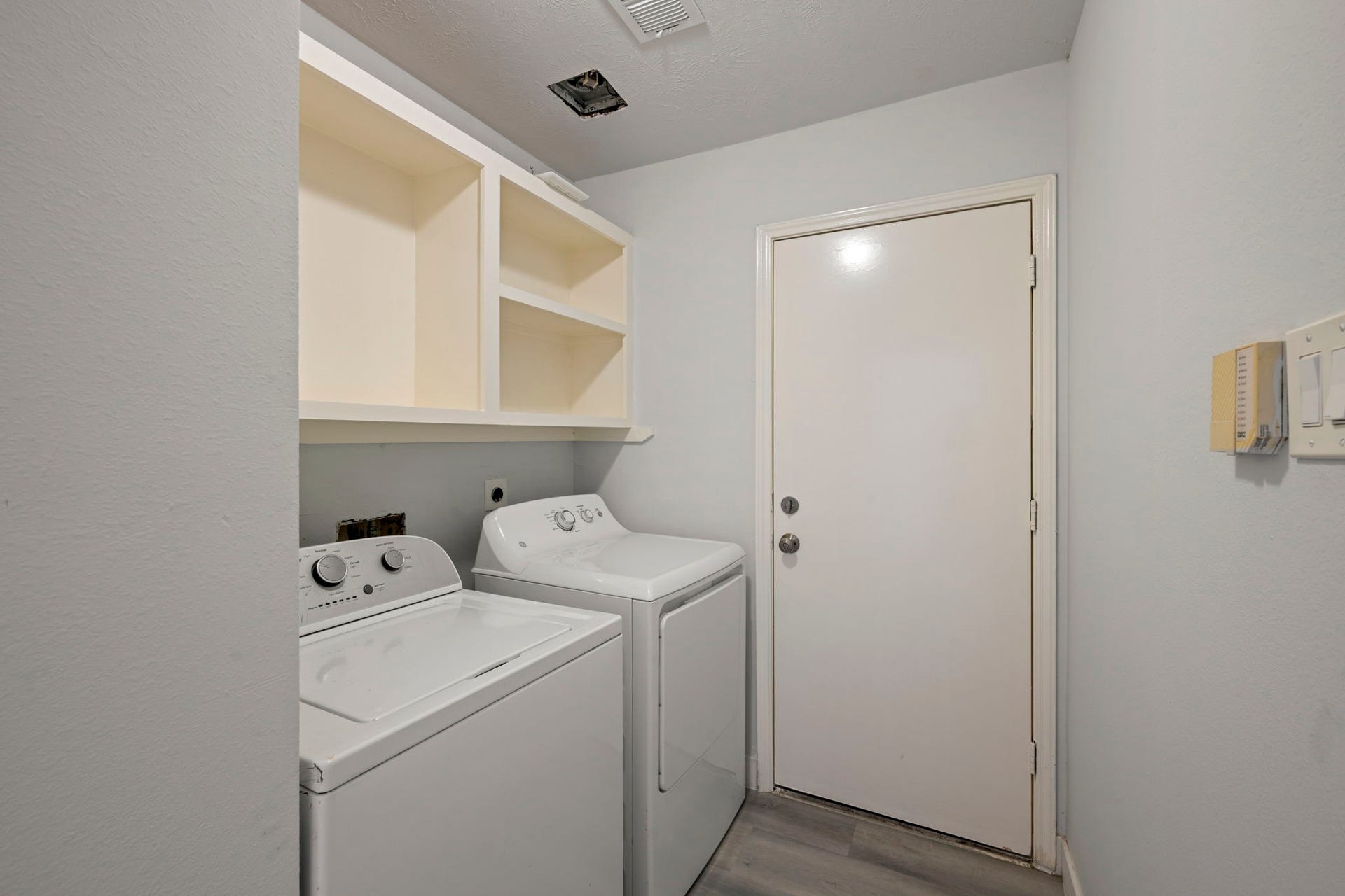 Convenient laundry room featuring a washer, dryer, overhead shelving, and an exterior door for easy access.