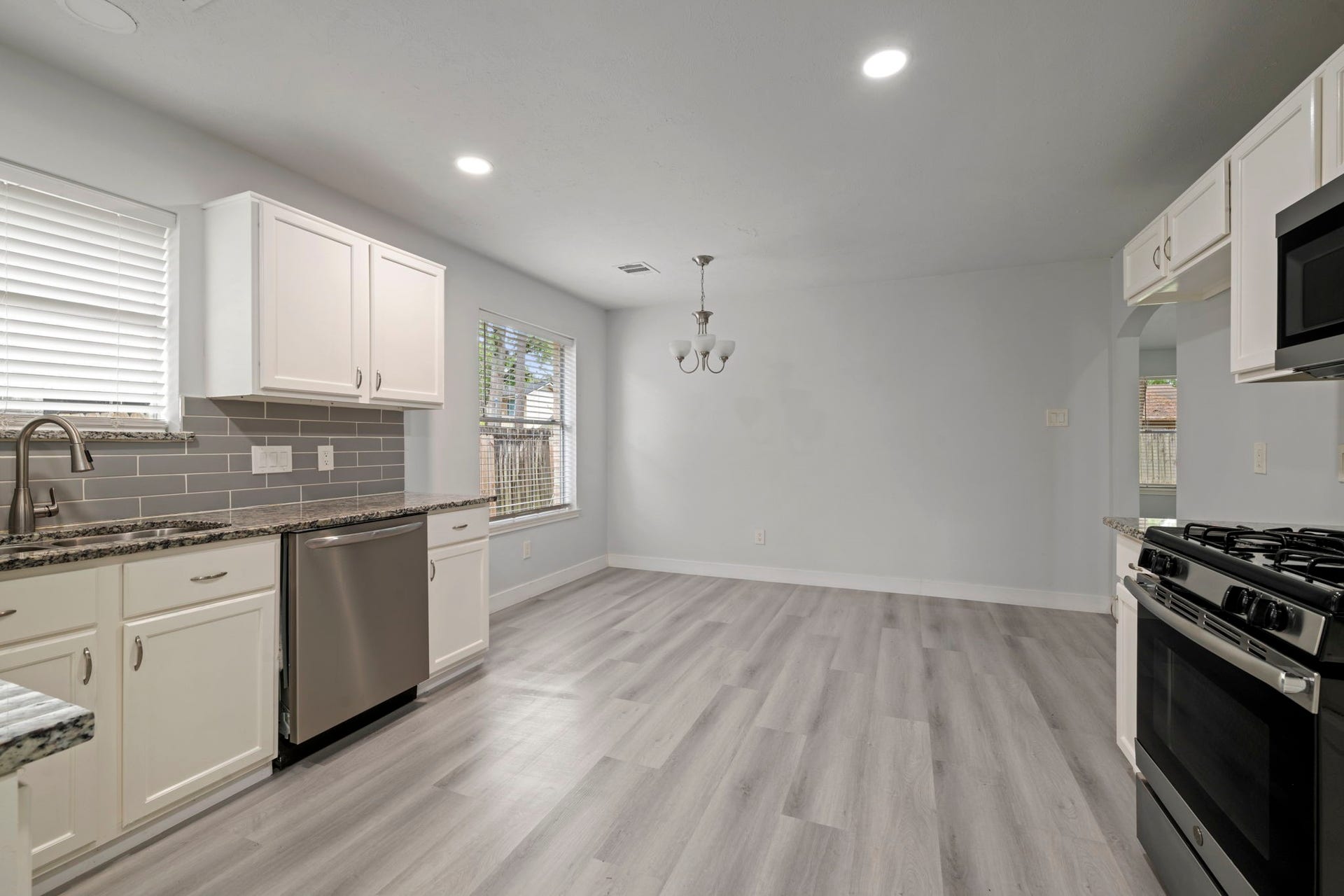 Modern kitchen with sleek stainless steel appliances, granite countertops, and elegant white cabinetry, seamlessly flowing into a spacious dining area with ample natural light.