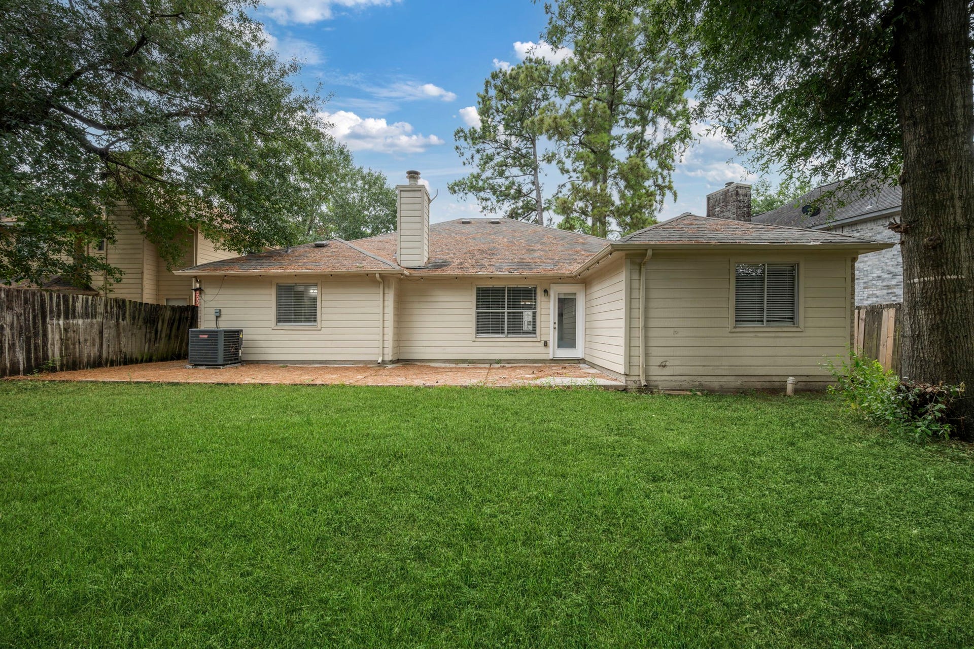 Charming single-story home with a spacious backyard, perfect for outdoor activities and entertaining, set against a backdrop of mature trees.