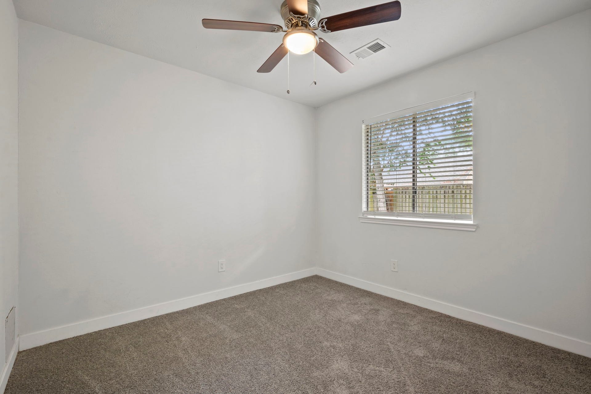 Cozy bedroom with soft carpeting, a ceiling fan for comfort, and ample natural light streaming through a large window.