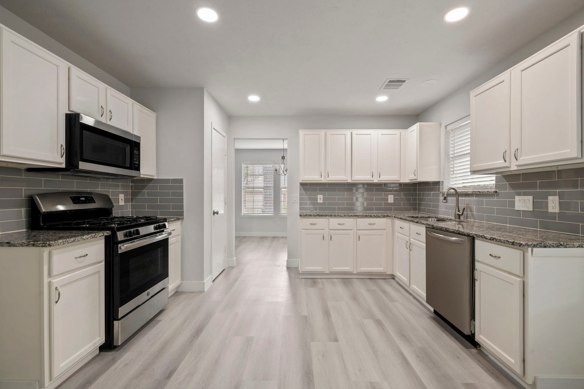 Spacious kitchen with sleek stainless steel appliances, elegant white cabinetry, and modern gray subway tile backsplash, offering a bright and inviting cooking space.
