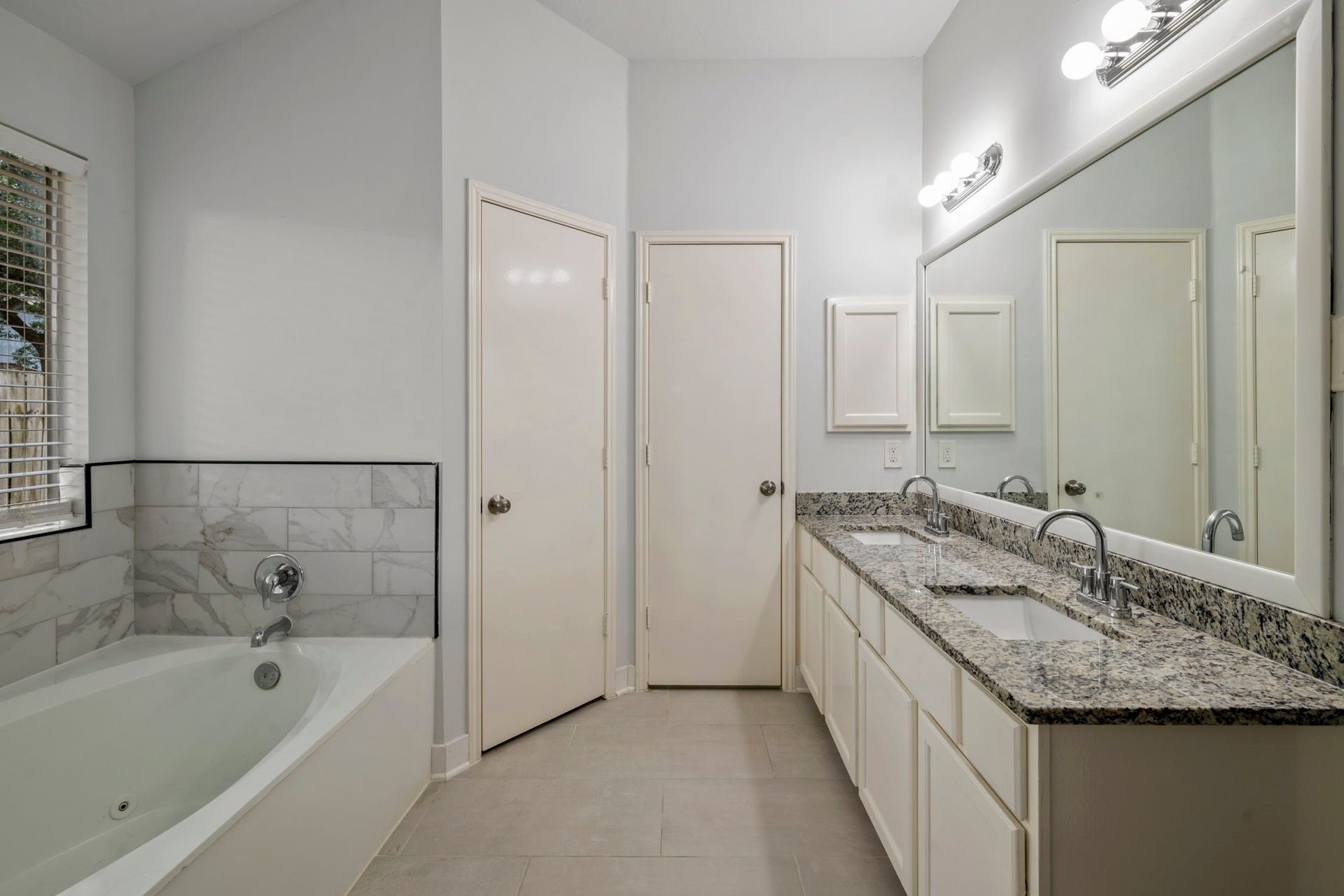 Elegant bathroom featuring a luxurious soaking tub, dual sinks with granite countertops, and ample storage space, all enhanced by soft, natural lighting.