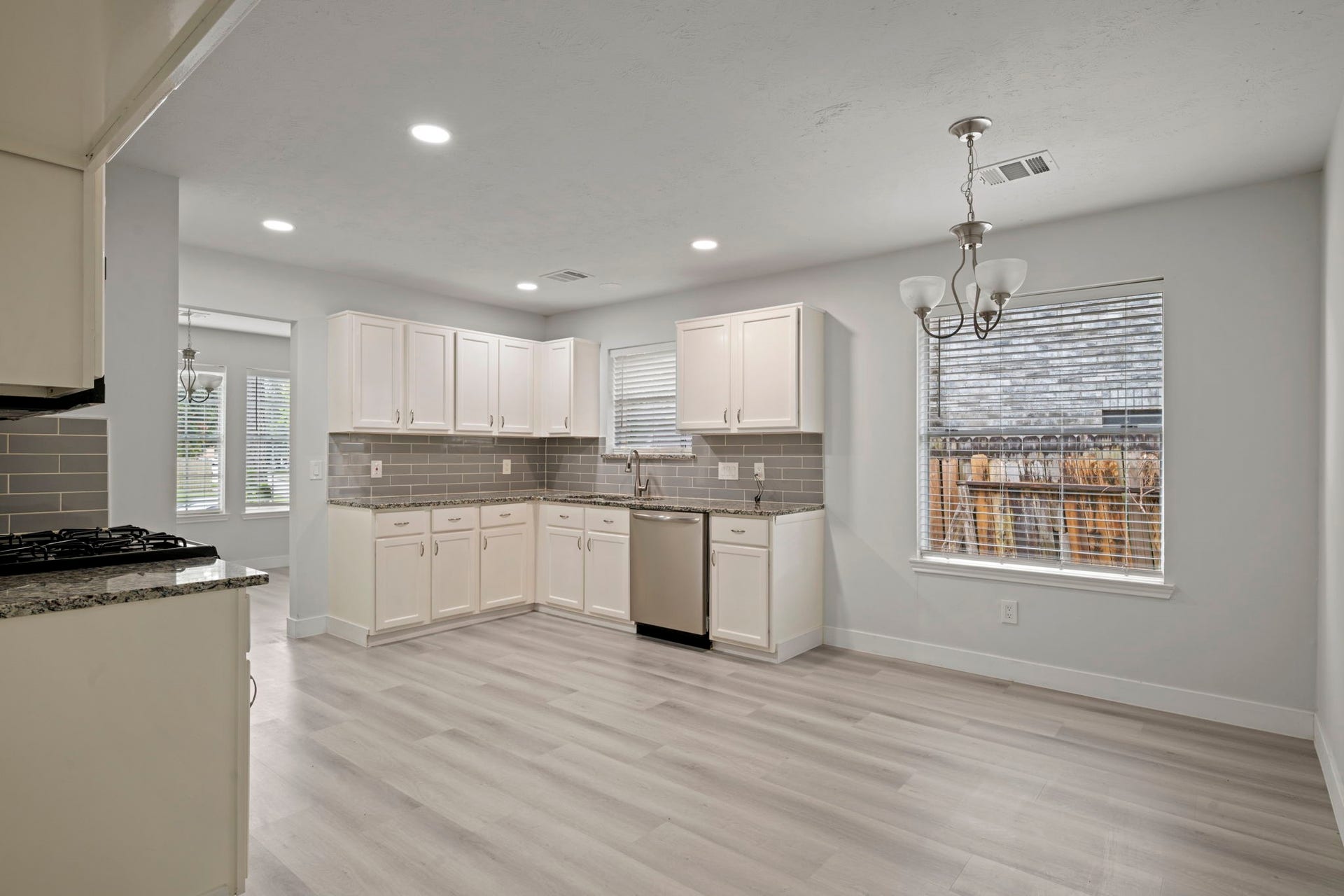 Bright and modern kitchen with sleek gray tile backsplash, stainless steel appliances, and elegant white cabinetry, complemented by light wood flooring and ample natural light.