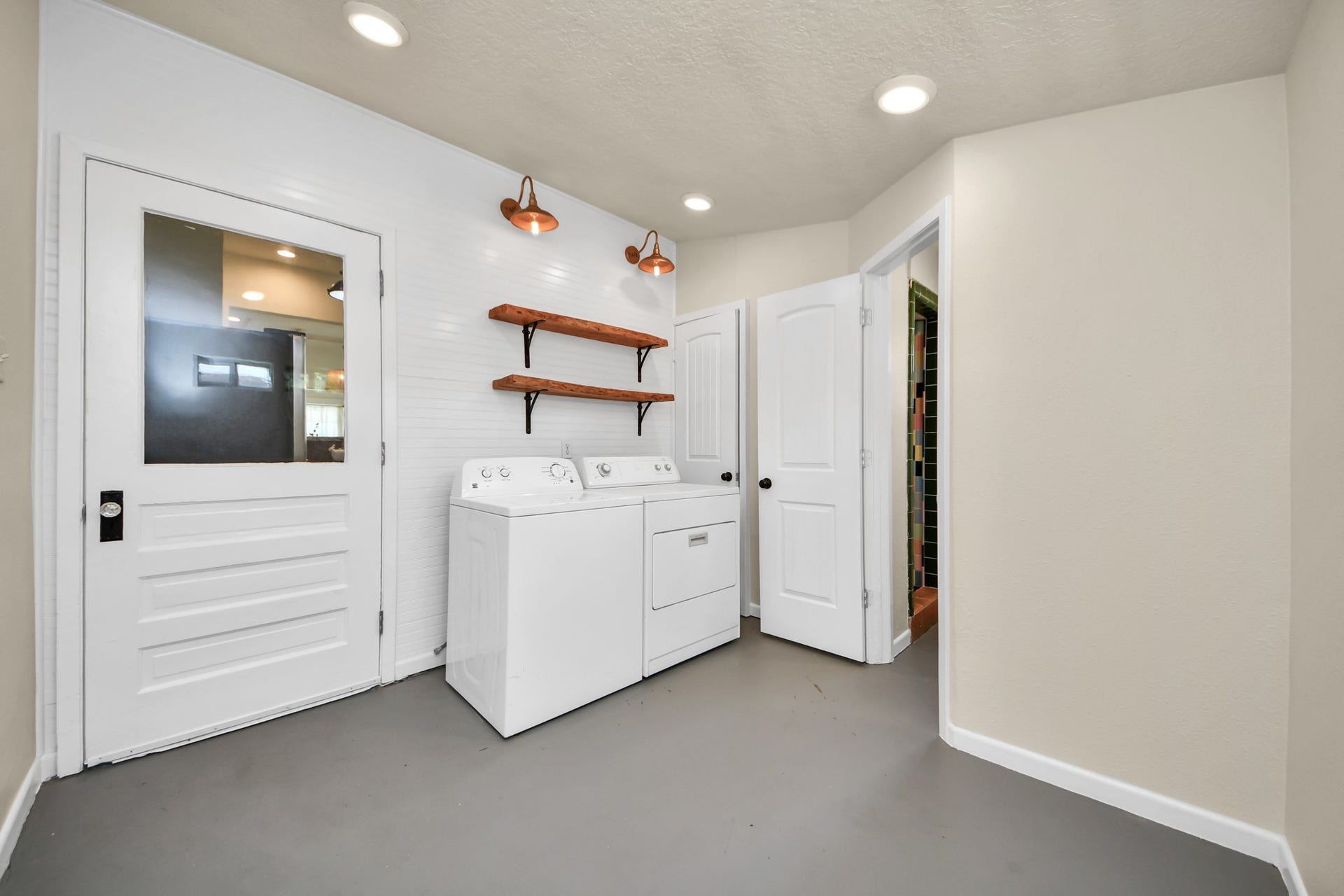 Generously sized laundry room featuring open wood shelving, charming copper barn lights, and direct access to the home.