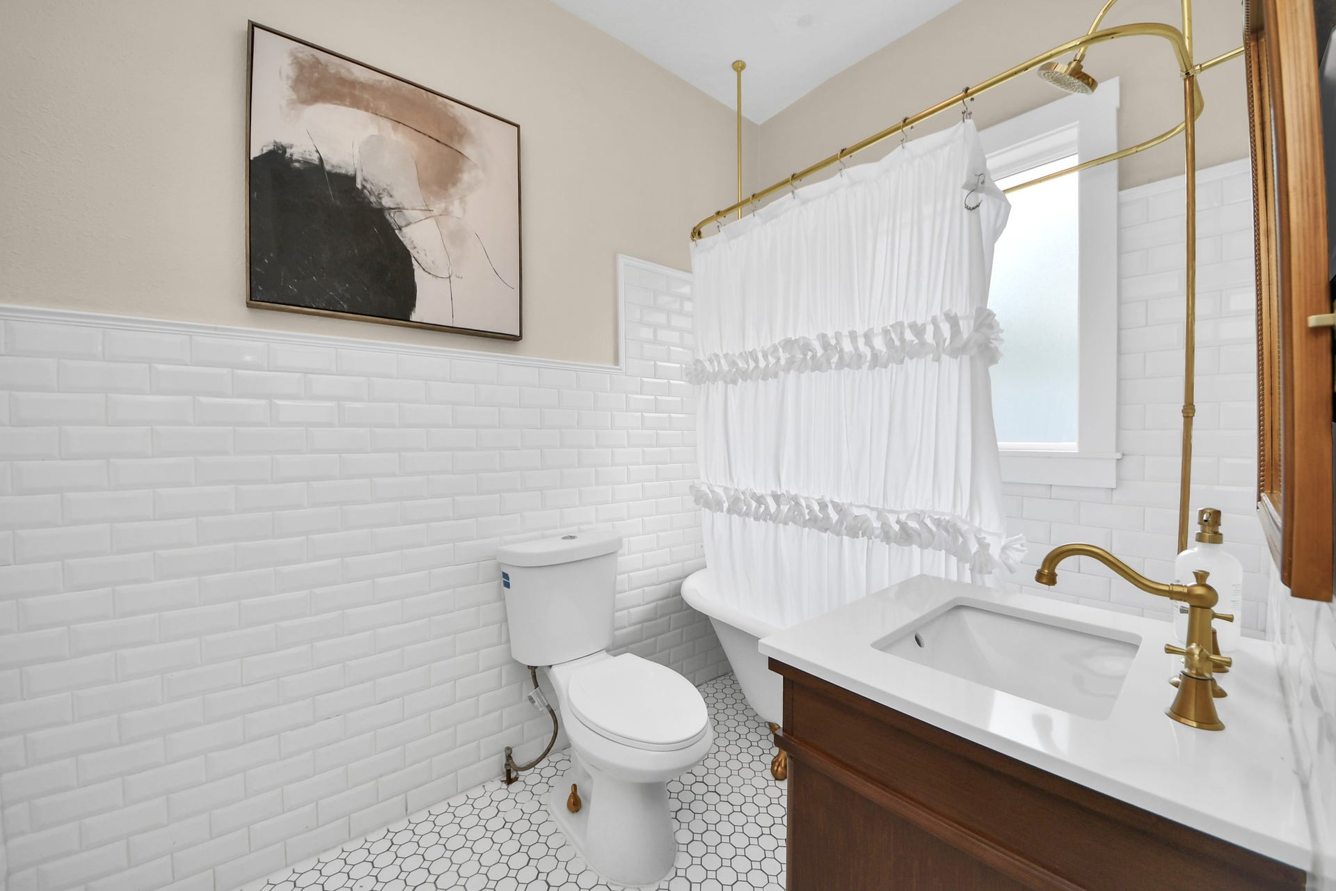 Timeless design shines in this bathroom, featuring classic white subway tile, hexagonal flooring, a vintage-inspired clawfoot tub, and a warm wood vanity with elegant brass fixtures.