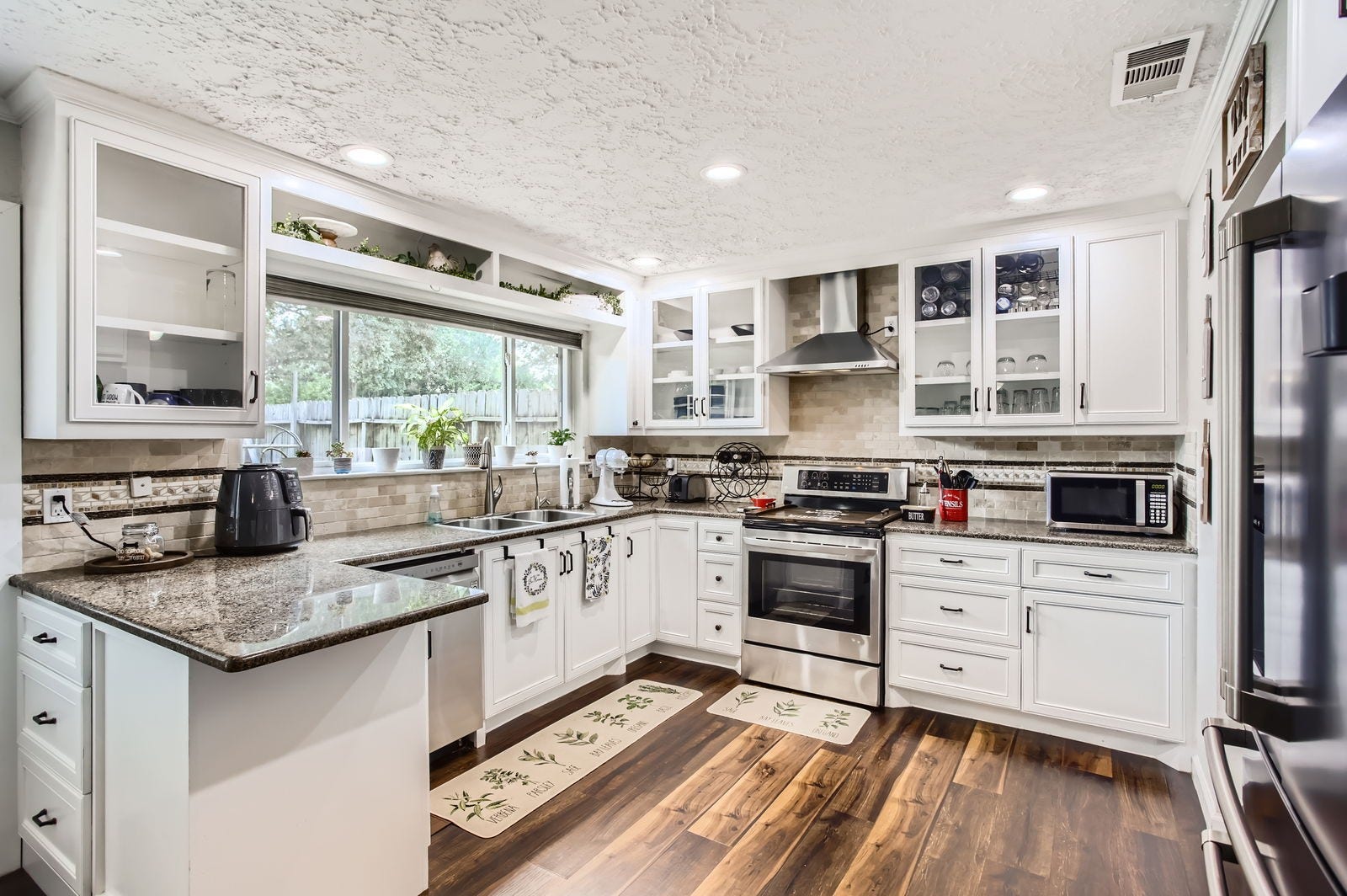 The heart of this home is definitely the kitchen, featuring granite countertops, custom stone backsplash, stainless steel appliances, bright glass front cabinetry and a panoramic window that lets the natural light pour in.