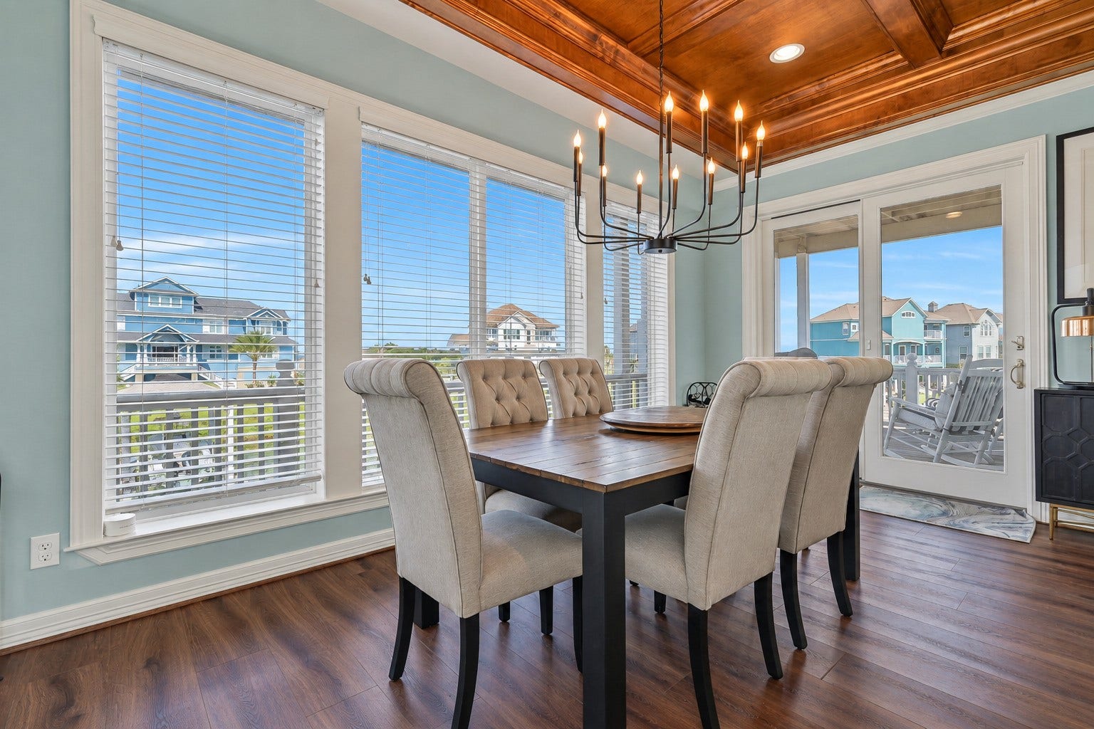 12 Fleming, Hitchcock, TX 77563 Dinner with a water view. The open-concept dining area sits at the heart of the main living floor, flowing seamlessly between the chef's kitchen and the connecting balconies beyond. Natural light pours in from every angle, and the hand-crafted coffered ceiling overhead makes every meal feel like an occasion.