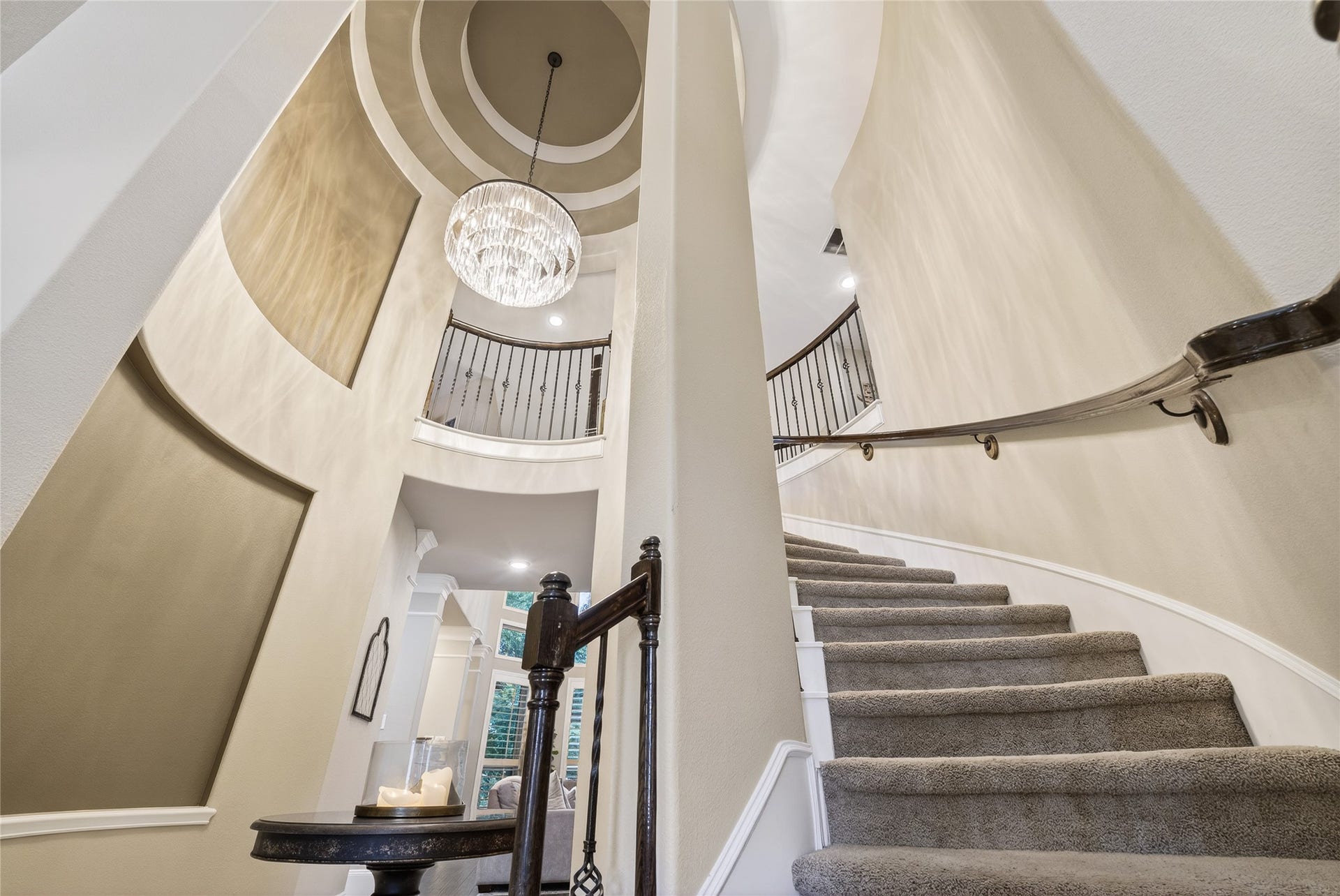 This home showcases a grand rotunda, curved staircase with elegant wrought iron railing and plush carpeting. A statement chandelier hangs from the high ceiling, adding a touch of luxury to the spacious foyer.