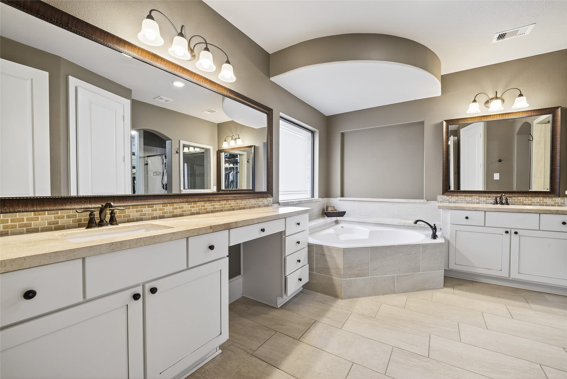 Enjoy escaping to this spacious bathroom featuring a fabulous soaking tub, dual sinks with large mirrors, elegant lighting, and ample cabinet space. What a serene and inviting atmosphere.