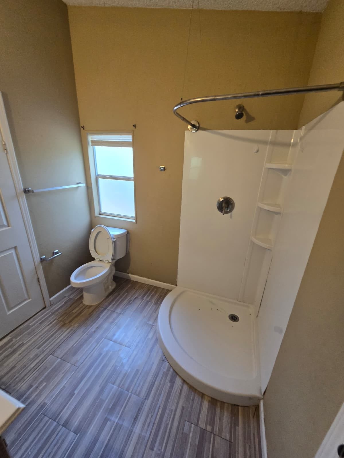Bright bathroom featuring a modern corner shower, stylish wood-look tile flooring, and a convenient window for natural light.