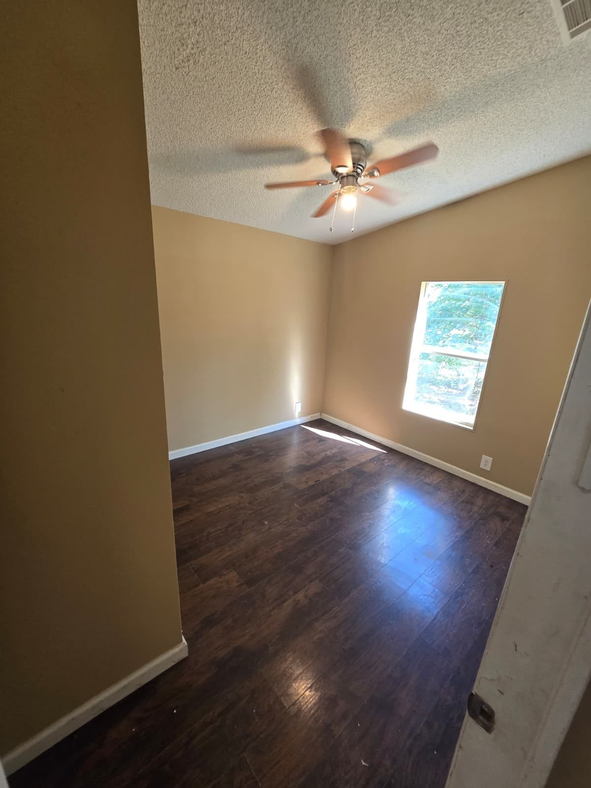 Cozy room featuring rich hardwood floors, a ceiling fan for comfort, and a bright window inviting natural light.