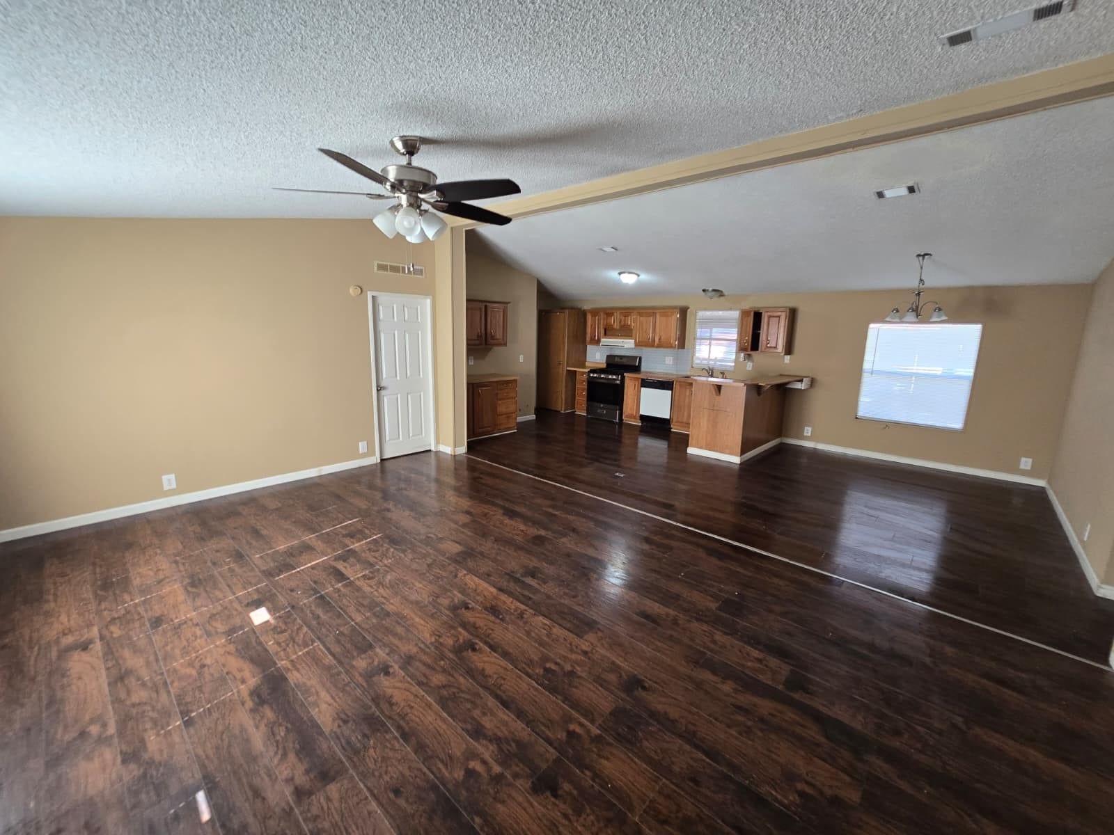 Spacious open-concept living area with rich hardwood floors, a ceiling fan, and an inviting kitchen featuring warm wooden cabinetry and modern appliances.
