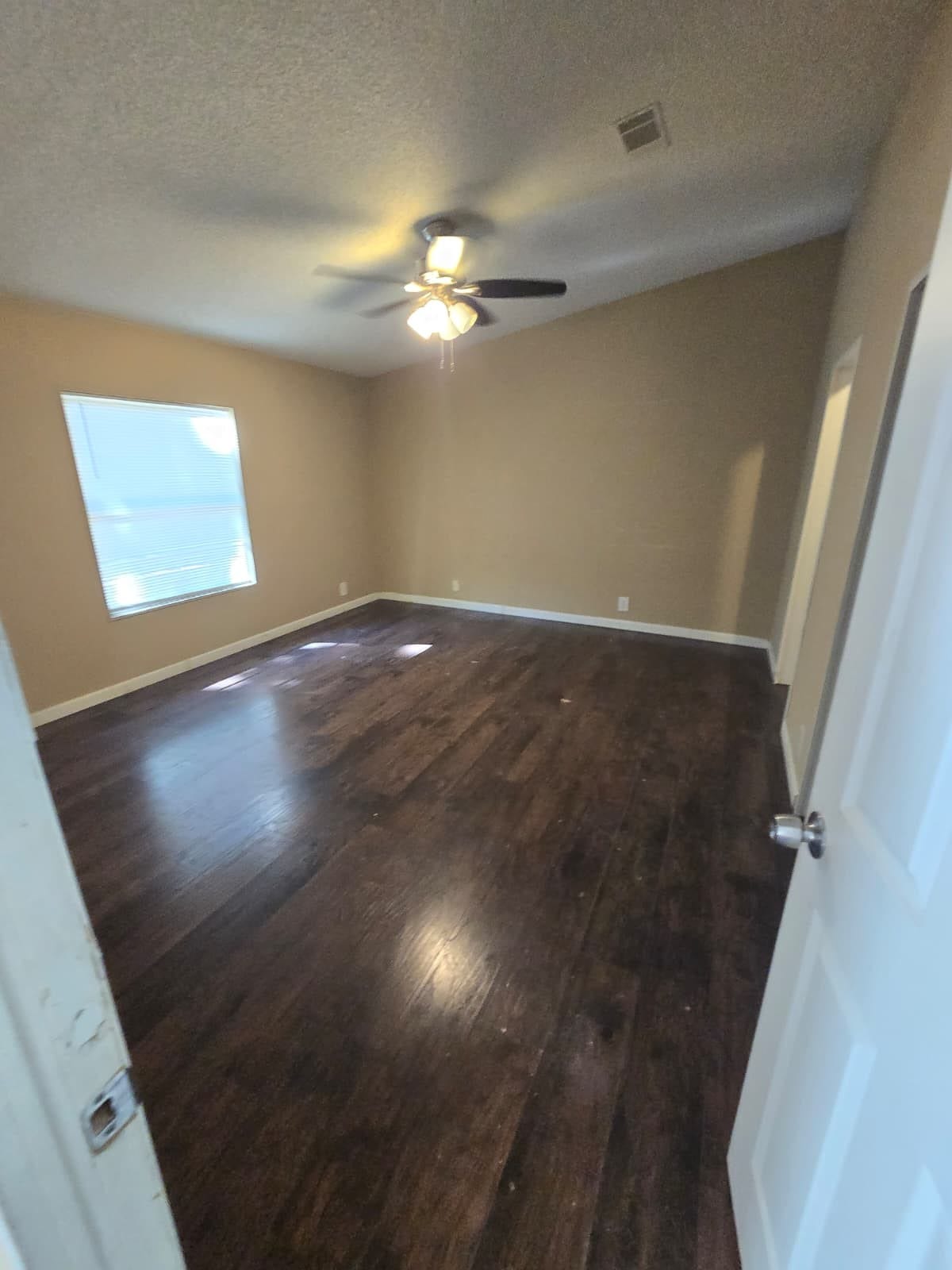 Spacious room featuring rich hardwood floors, a ceiling fan for comfort, and a large window inviting natural light.