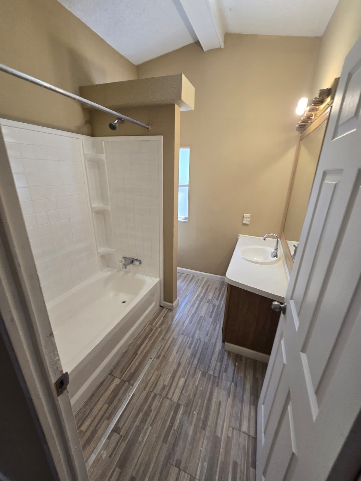 Charming bathroom with a vaulted ceiling, featuring a bathtub with shower, modern wood-look tile flooring, and a sleek vanity.