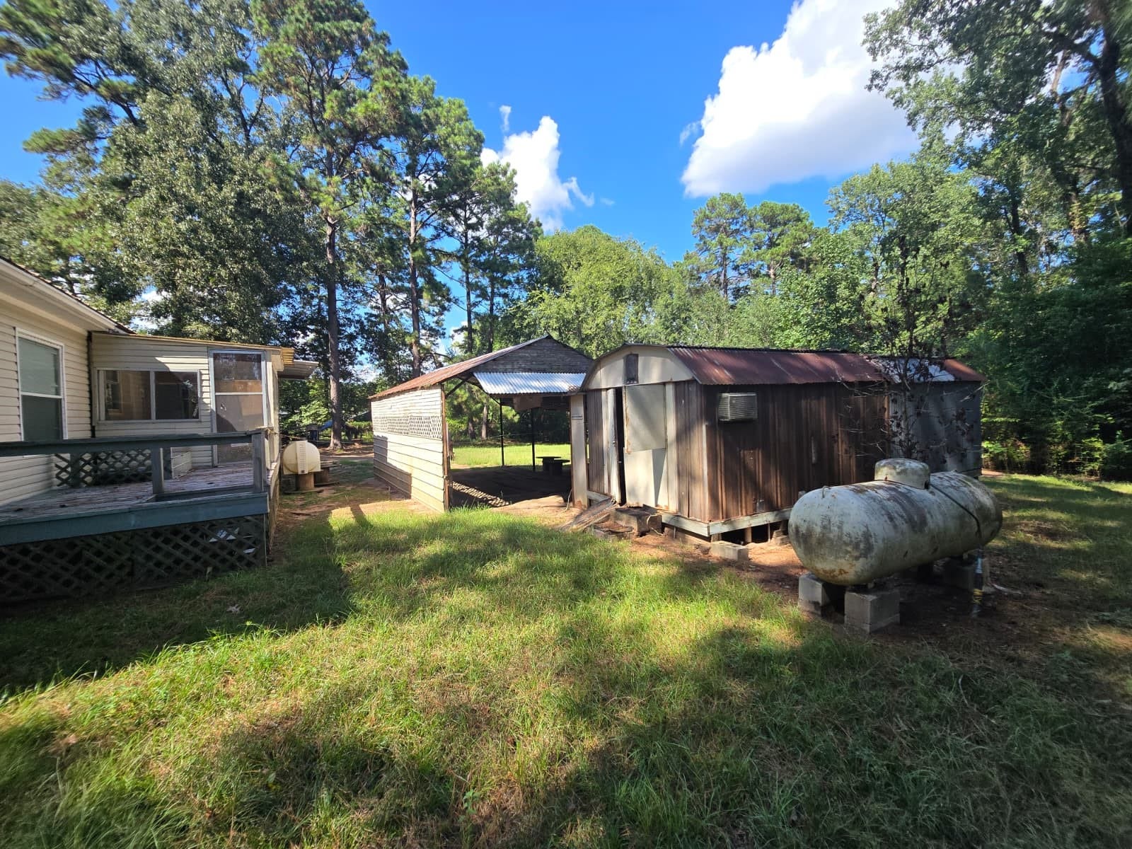 Spacious backyard with rustic outbuildings and a cozy deck, surrounded by lush greenery and mature trees. Perfect for outdoor enthusiasts seeking tranquility.