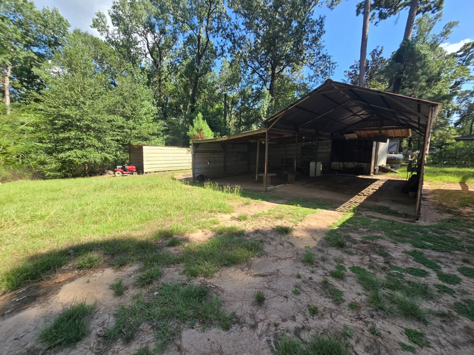 Expansive backyard with a large covered carport and additional storage shed, surrounded by mature trees for added privacy.