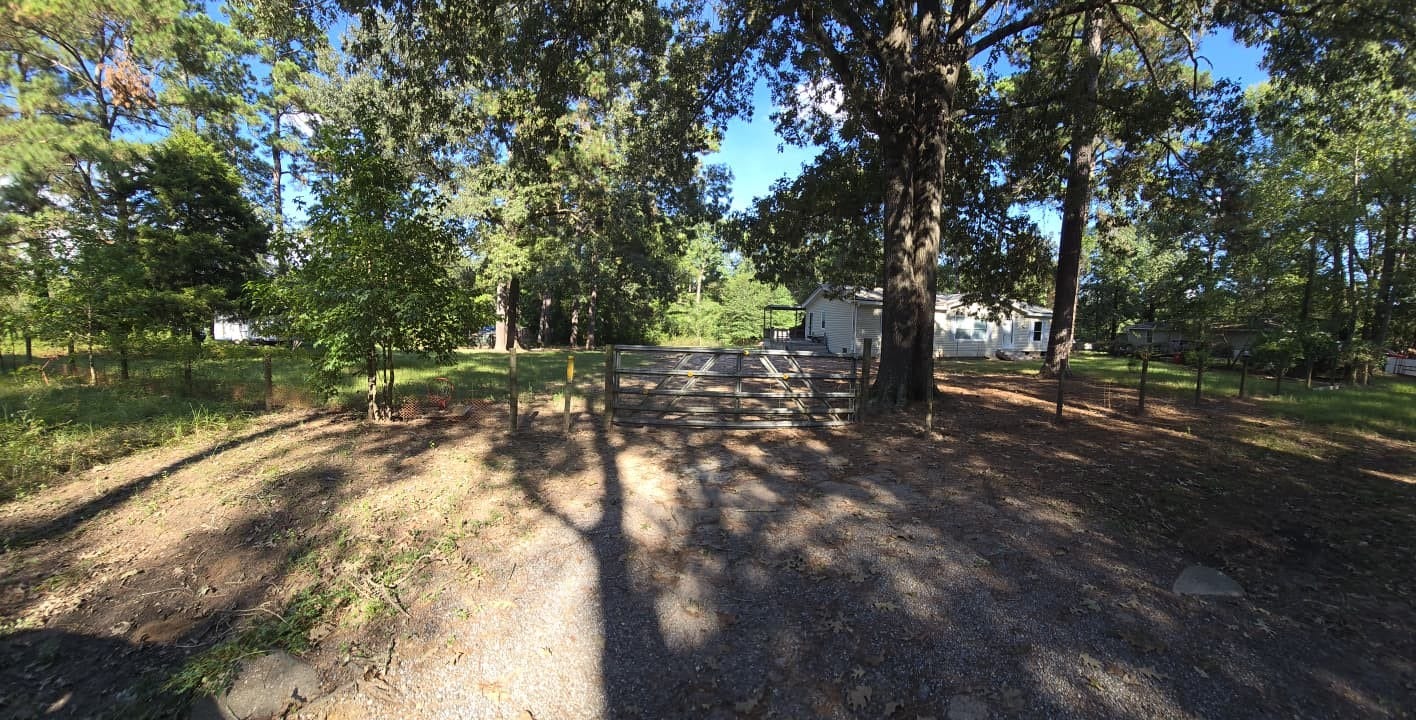 Charming rural property with a gated entrance, surrounded by mature trees and lush greenery, leading to a cozy home nestled in nature.