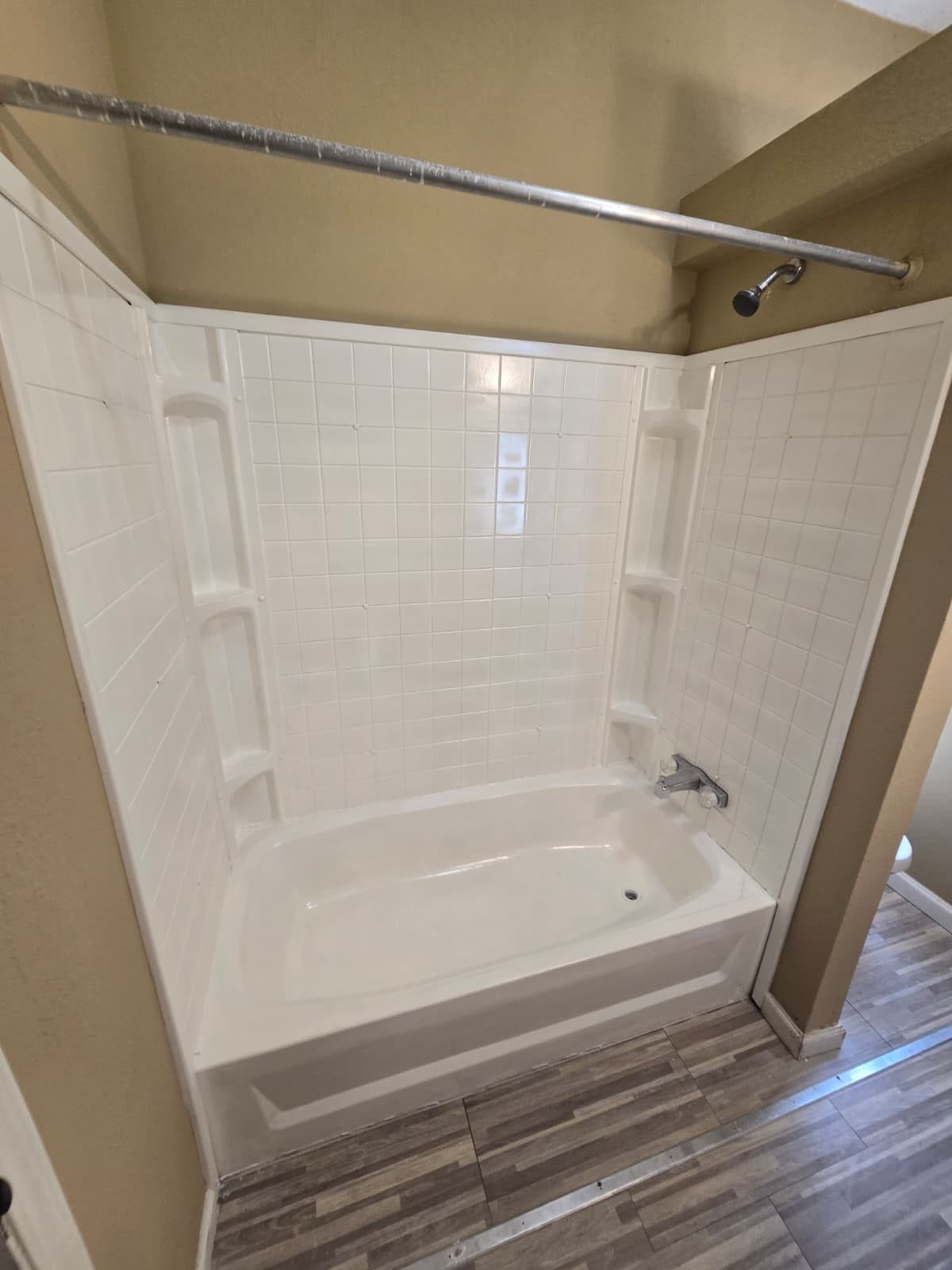 Bright bathroom featuring a clean white bathtub with tiled walls and modern wood-look flooring.