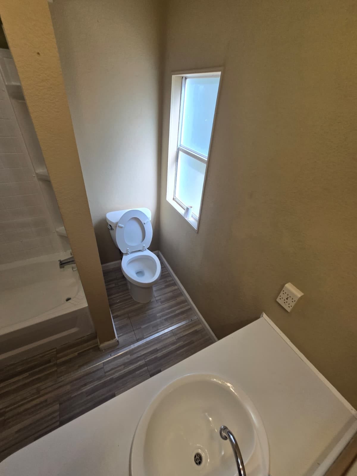 Compact bathroom with modern fixtures features a bathtub, toilet, and a sleek sink under natural light from a frosted window.