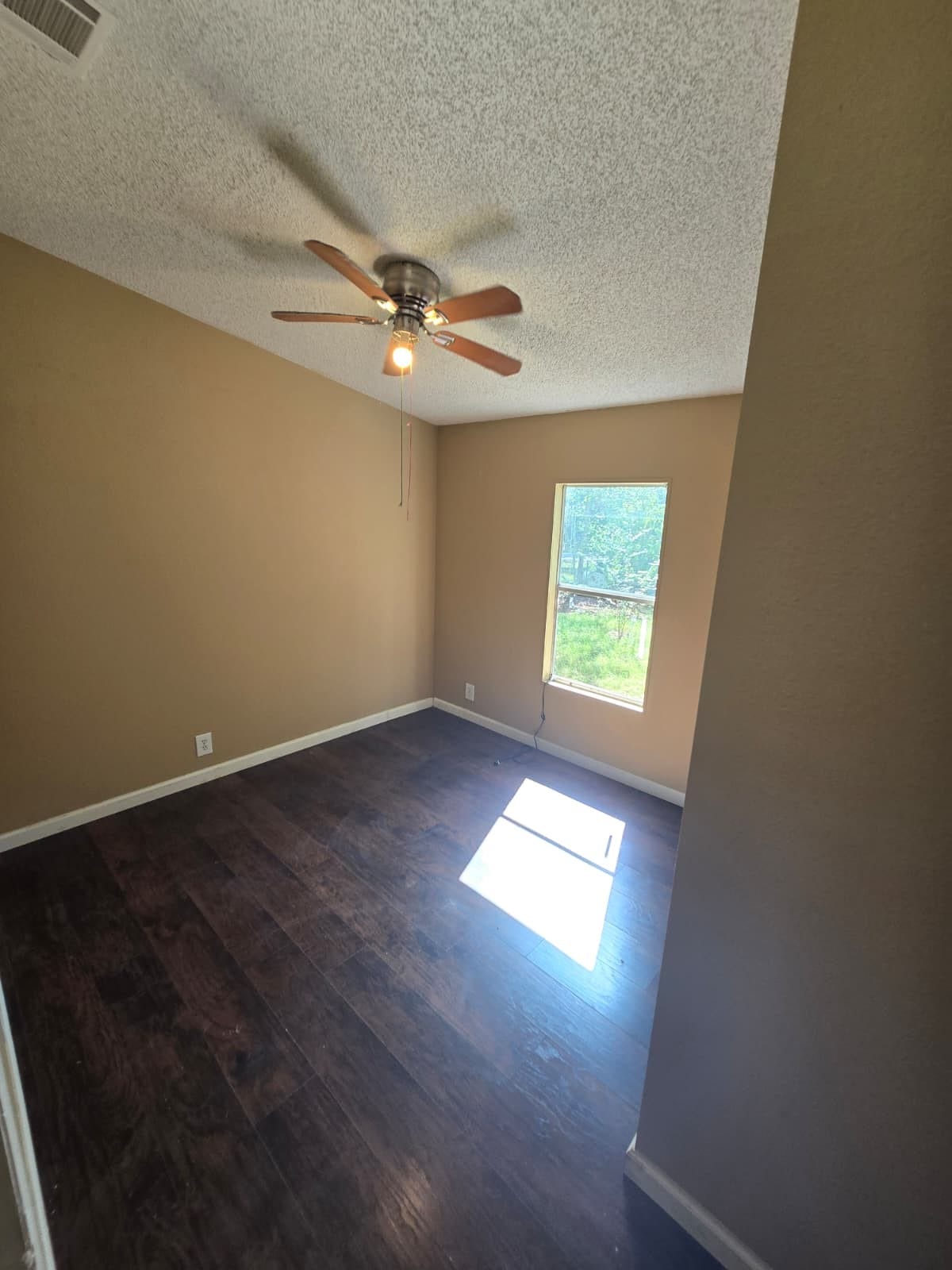 Cozy room with rich wood flooring, a ceiling fan, and ample natural light from a large window.