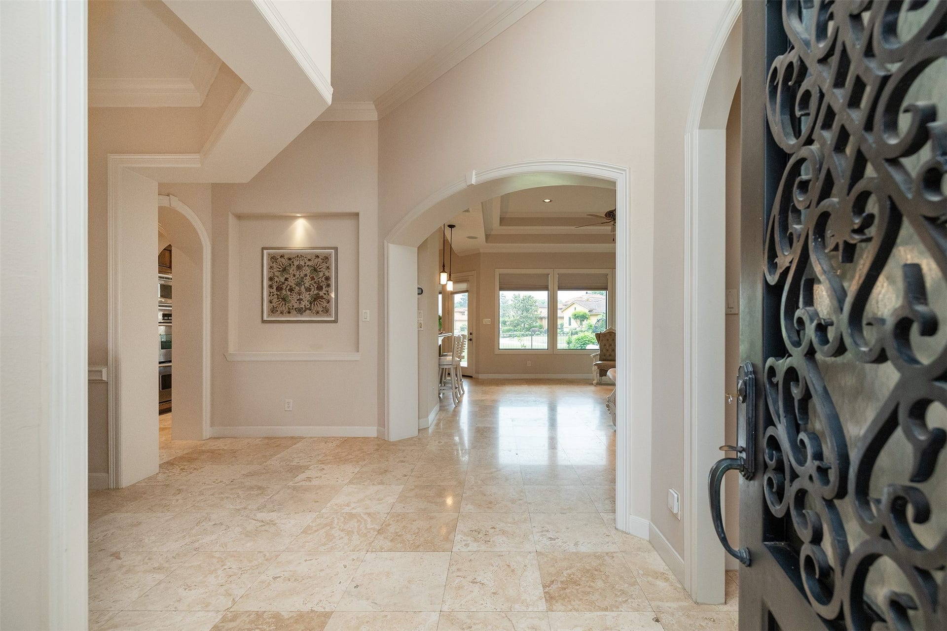 Welcome to a spacious and elegant entryway with polished stone flooring, high ceilings, and decorative arches. The open layout leads to a bright living area with large windows that offer scenic views, creating a warm and inviting atmosphere.