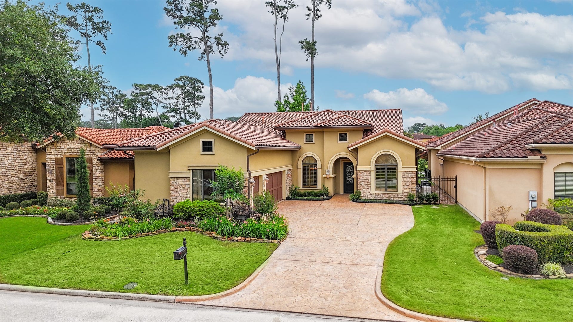 This beautiful home features a Mediterranean-style design with a red-tiled roof and a blend of stone and stucco exterior. It boasts a spacious, landscaped front yard and a wide driveway leading to a two-car garage, offering excellent curb appeal.