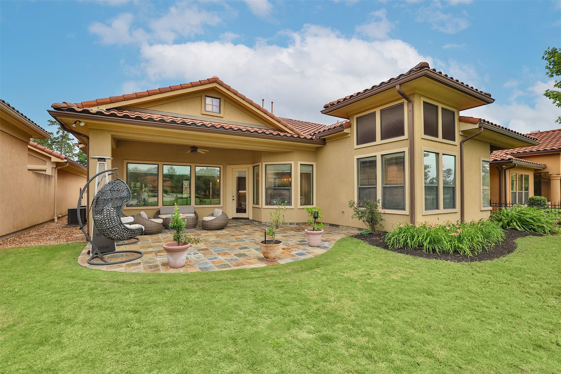 Charming home with a spacious, landscaped backyard featuring a tiled patio, comfortable outdoor seating, and a stylish hanging chair. Ideal for relaxation and entertaining.