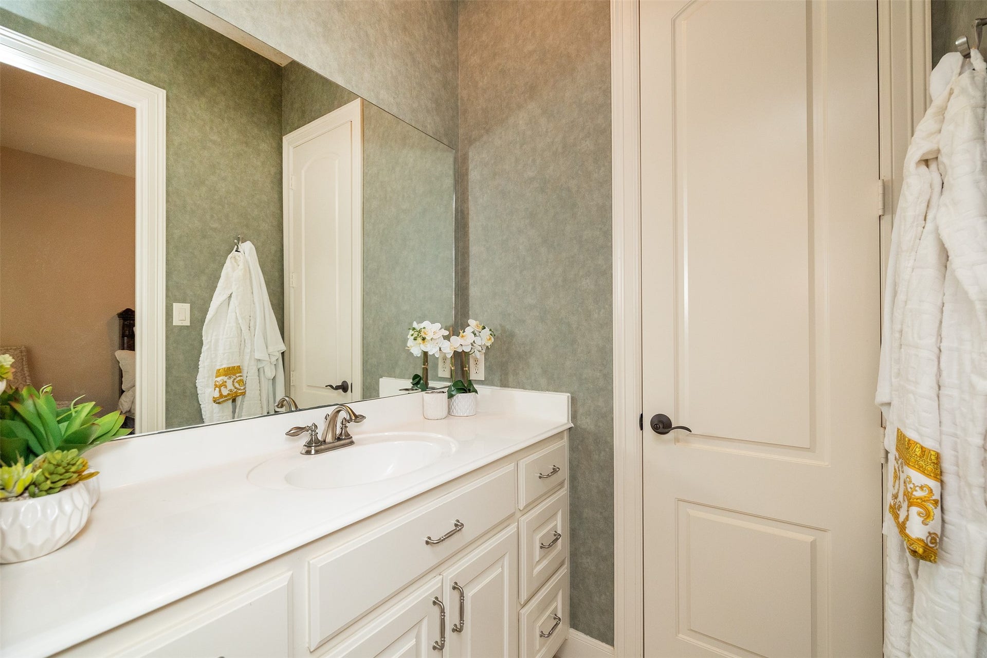 This bathroom features a sleek white vanity with ample storage, a large mirror, and stylish fixtures. It has a neutral color scheme, adding elegance and warmth to the space.