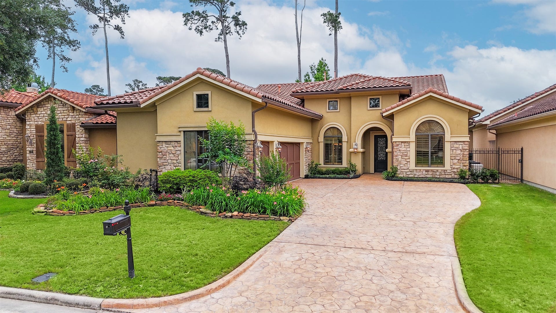 This charming home features a Mediterranean-style exterior with a terracotta tile roof and stone accents. It has a welcoming arched entrance, a beautifully landscaped front yard, and a spacious driveway. The property exudes warmth and elegance, ideal for comfortable living.