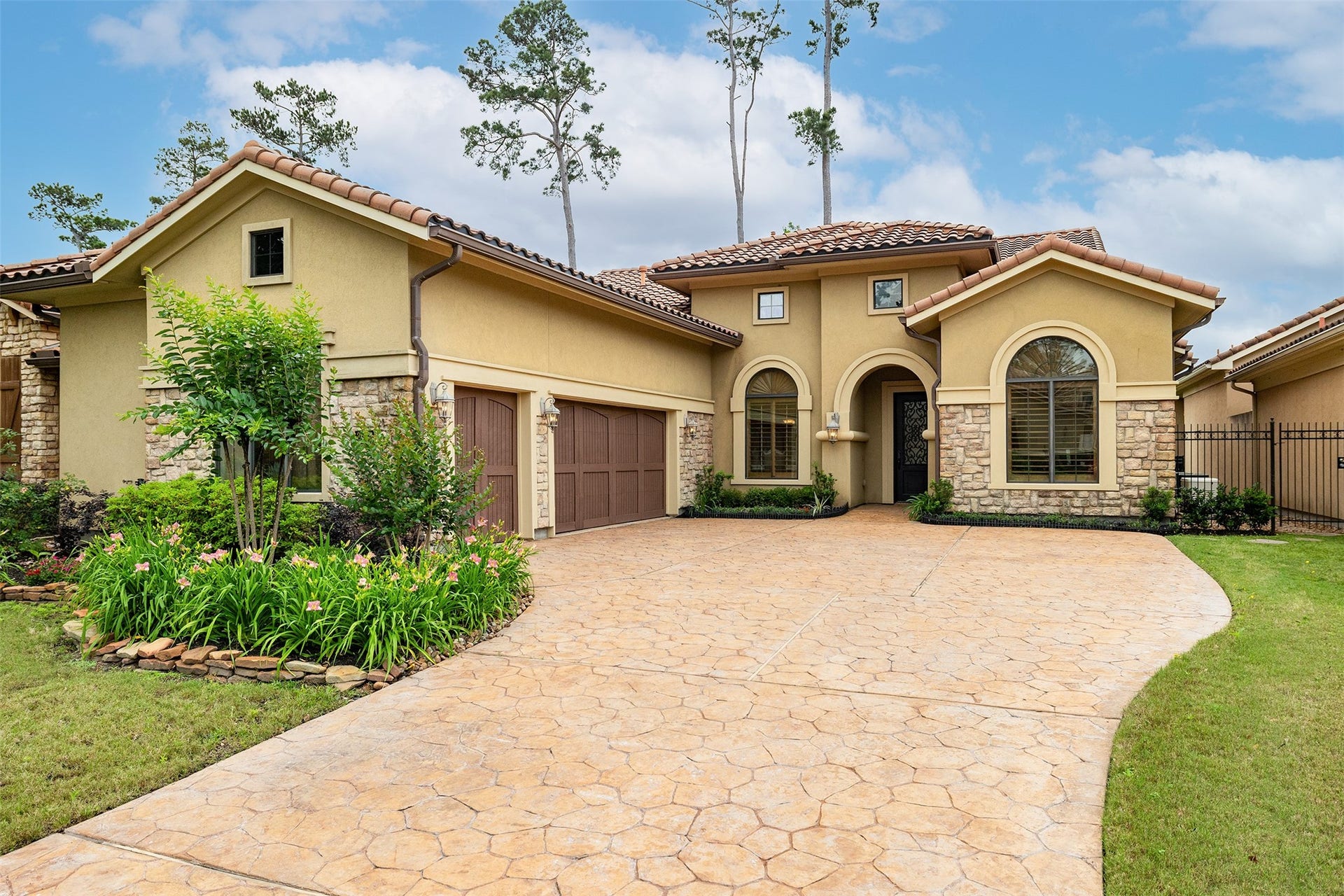 This charming home features a stucco and stone exterior with a tile roof, a spacious driveway, and lush landscaping. The large arched windows and elegant entryway create a welcoming facade.