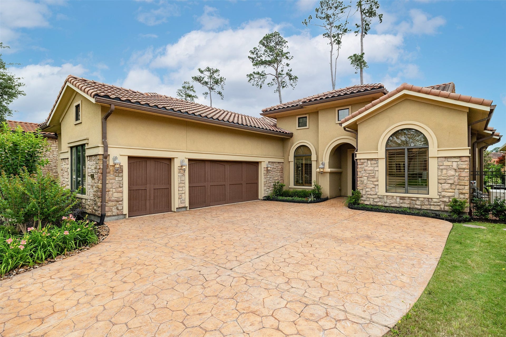 This photo showcases a beautiful Mediterranean-style home with a stone and stucco facade, a three-car garage, and a welcoming arched entryway. The property features a spacious driveway and well-maintained landscaping, offering great curb appeal.