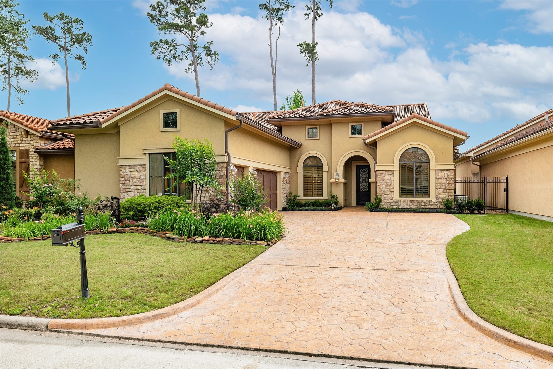 This stunning home features a Mediterranean-style exterior with a blend of stucco and stone accents. It has a beautifully landscaped front yard, a spacious driveway, and elegant arched windows. The tiled roof and warm earth tones create an inviting curb appeal.