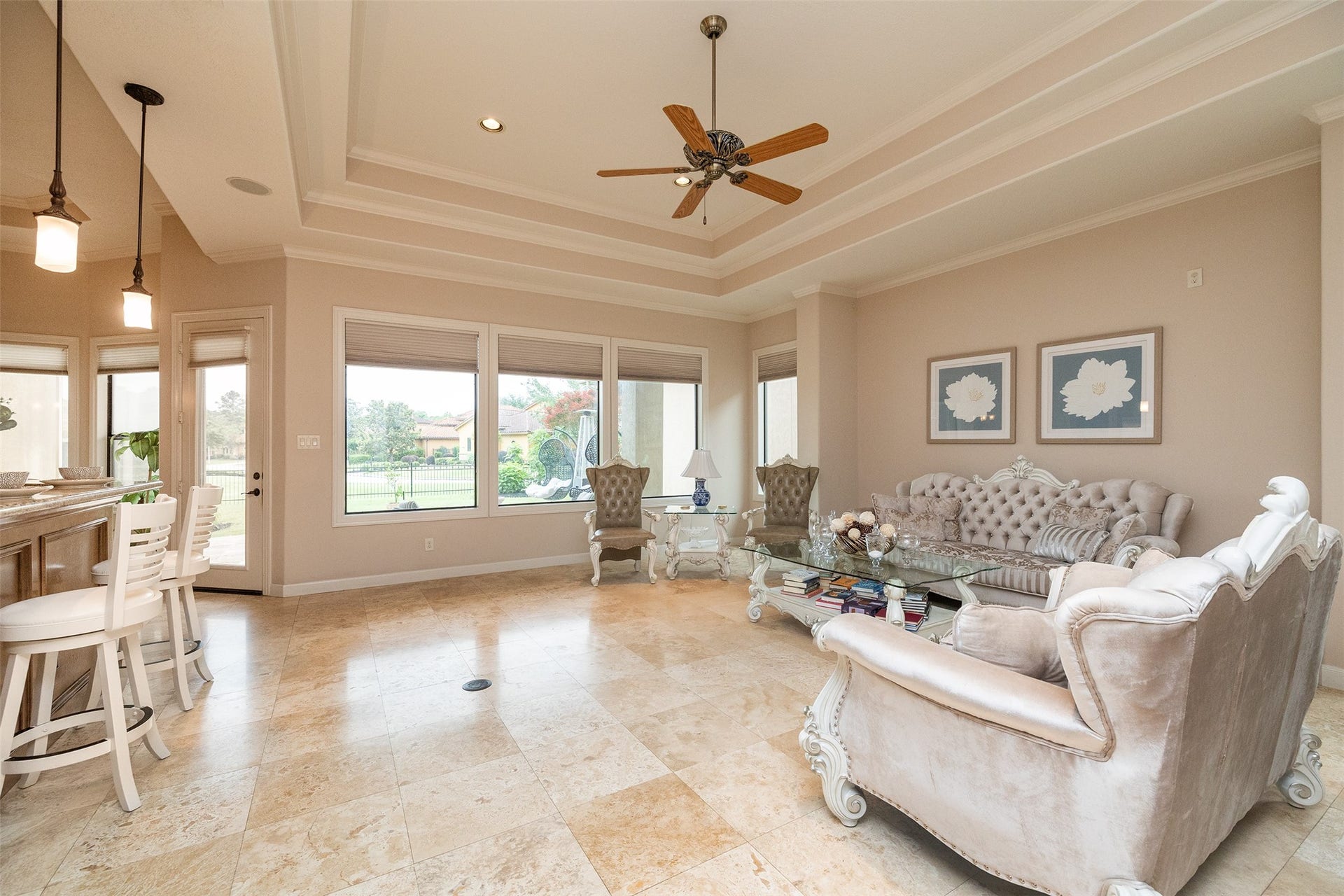 This spacious living room features elegant furnishings, tile flooring, and large windows offering plenty of natural light. The open layout includes a ceiling fan and access to a patio, providing a seamless indoor-outdoor living experience.