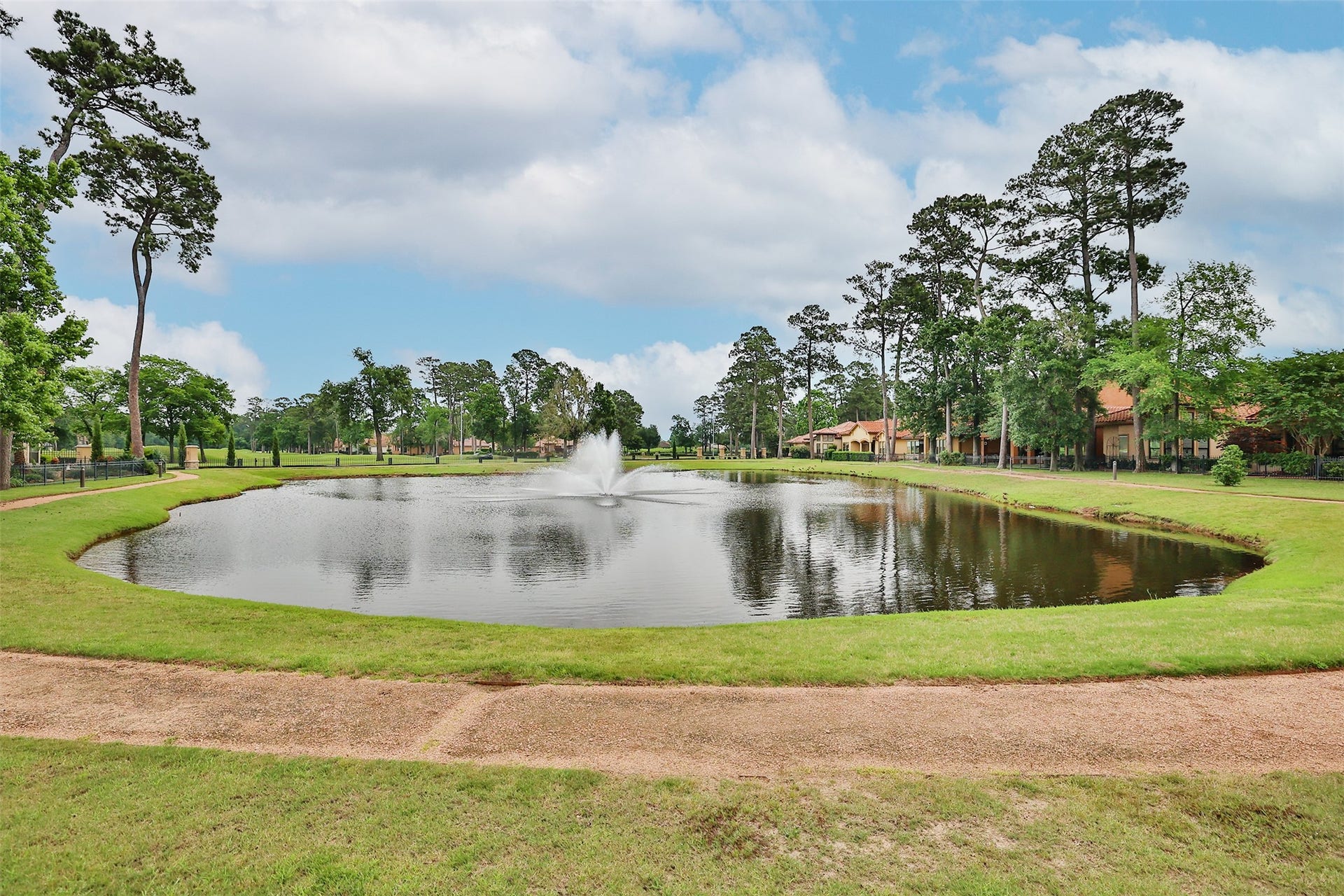 This photo showcases a serene neighborhood pond with a central fountain, surrounded by lush greenery and tall trees, creating a peaceful and picturesque setting ideal for nature lovers.